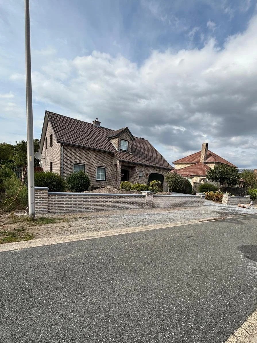 Een huis onder constructie met een nieuwe muur en bestrating, met een grijze lucht erboven.