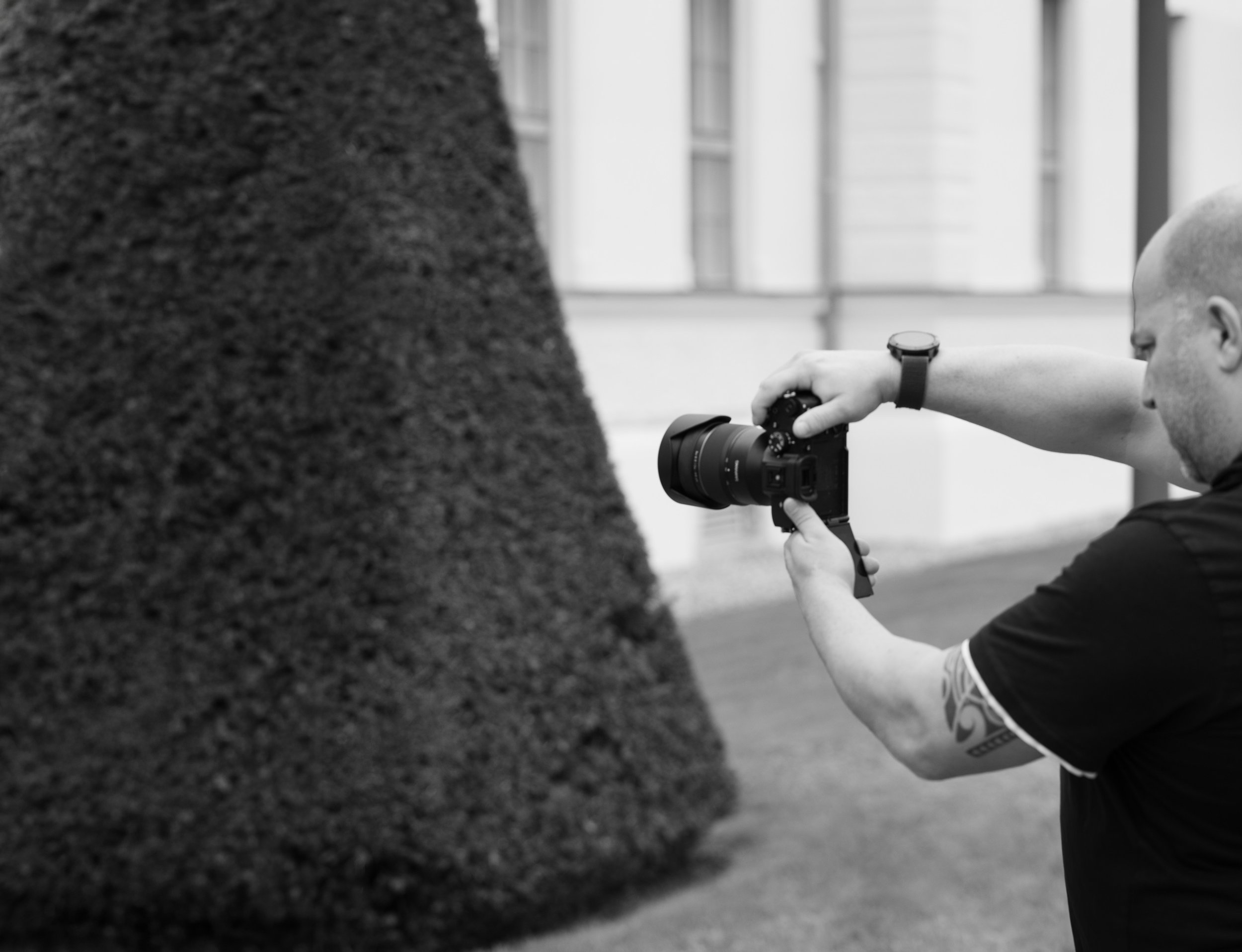 Workshop. Mann fotografiert ein Objekt mit einer Kamera in einem Gebäude mit großen Fenstern im Hintergrund. Portrait- und Cinematic-Fotografie von Lux Capere