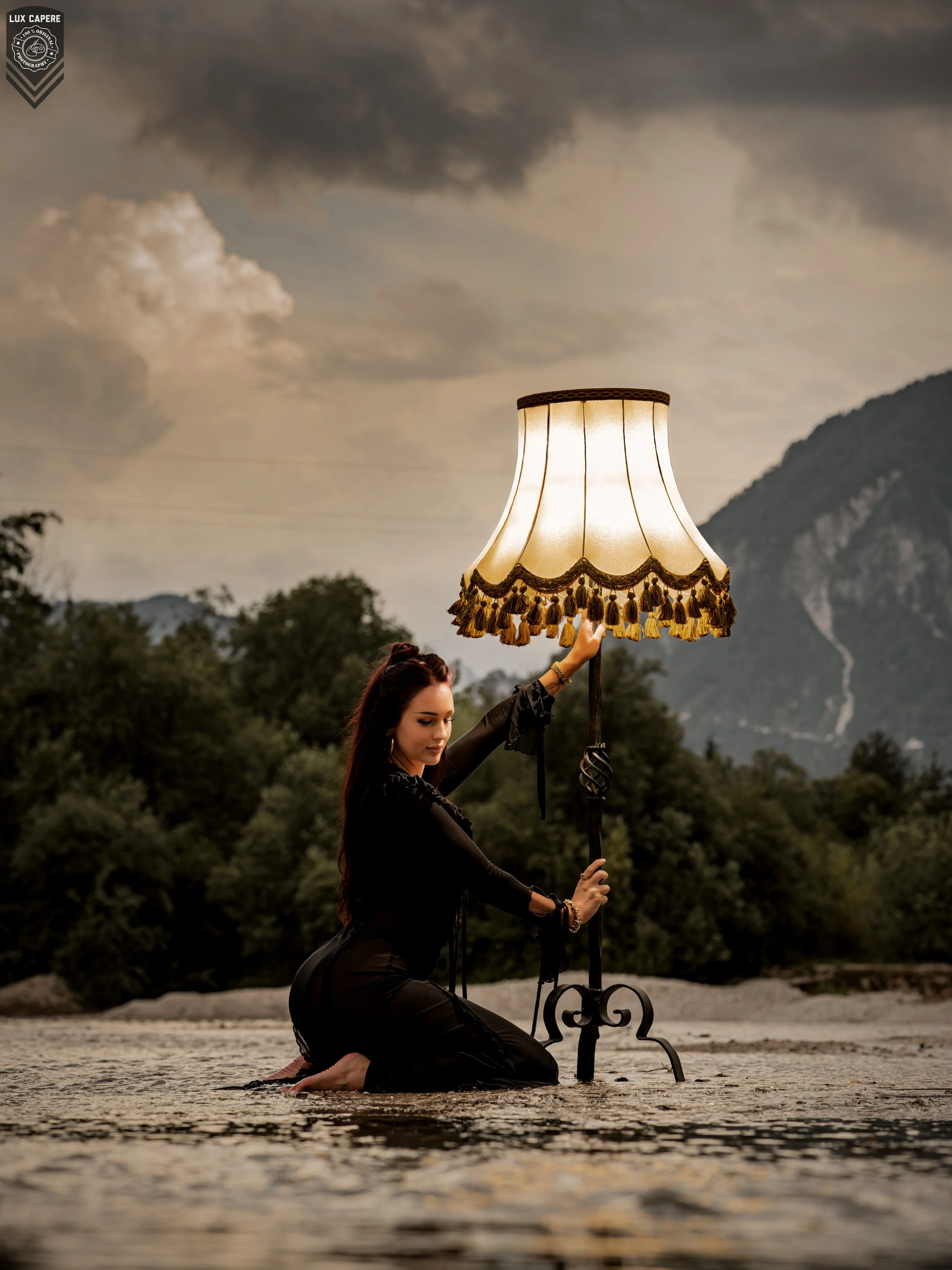 Frau hält Lampenschirm bei Sonnenuntergang in einem Fluss. Portrait- und Cinematic-Fotografie von Lux Capere