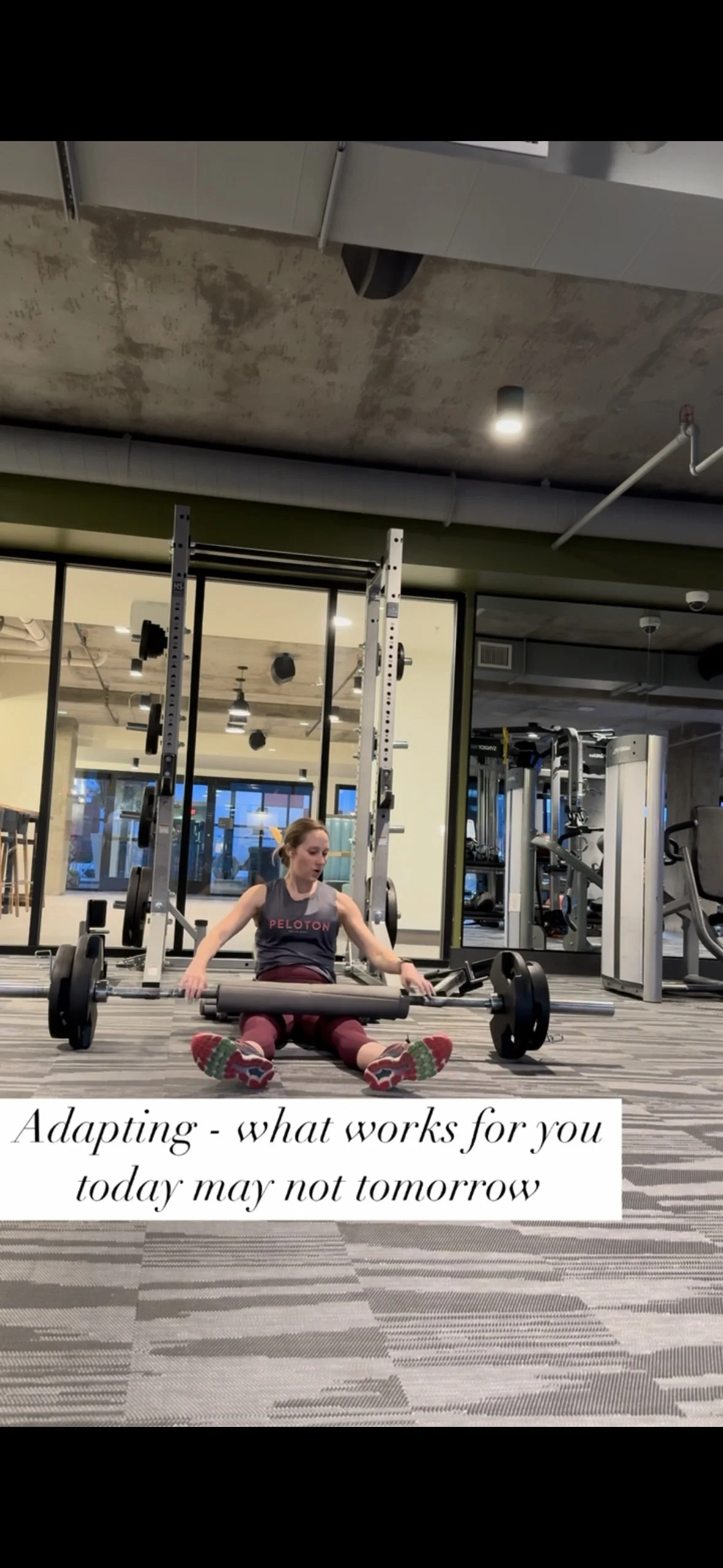 Young woman sitting on the gym floor with a barbell and weights, in a modern gym with workout equipment and large windows. Text overlay reads: 'Adapting - what works for you today may not tomorrow.'