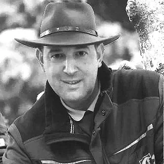 A man wearing a cowboy hat and outdoors, smiling at the camera.