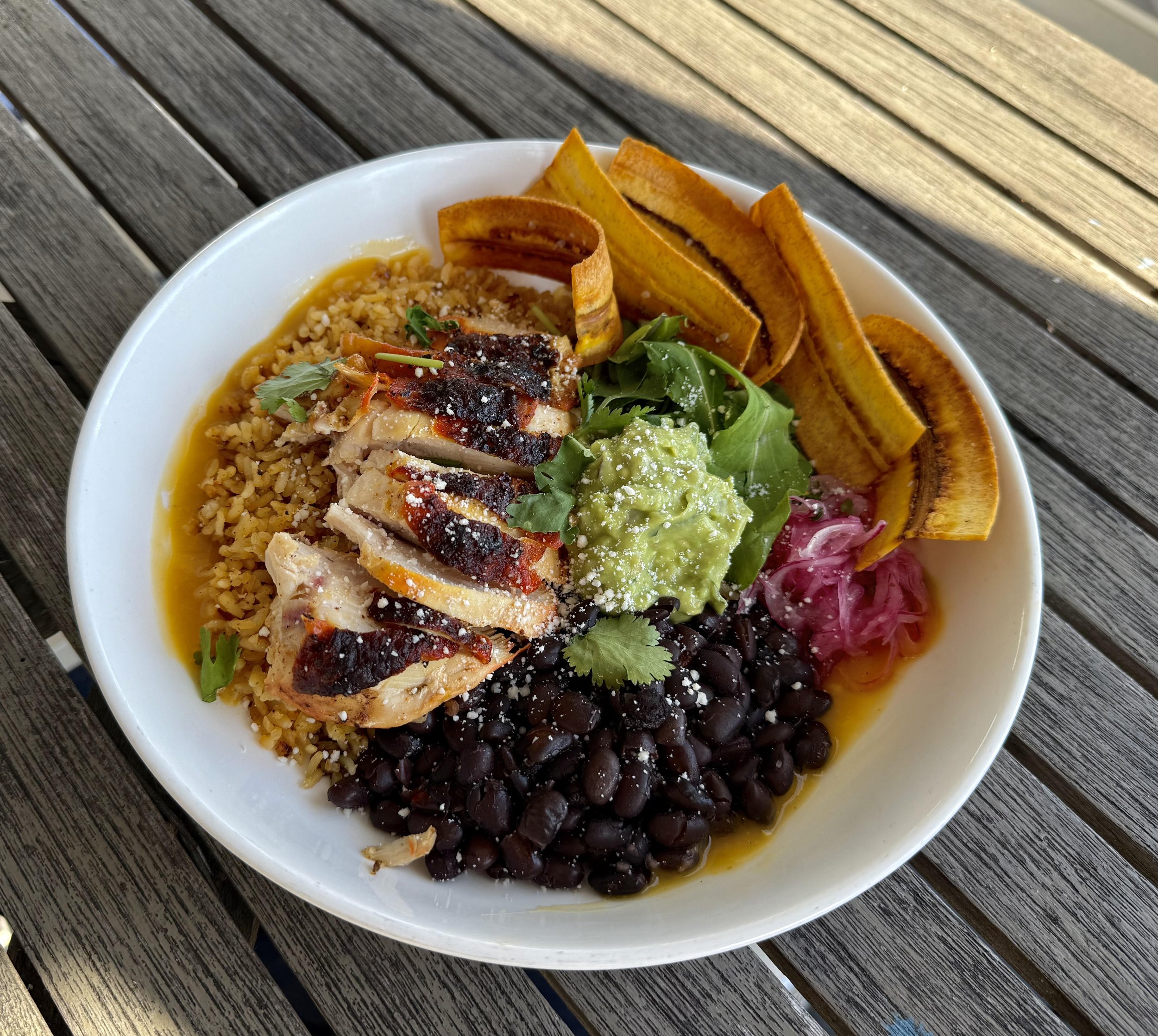 Chicken and rice bowl with skin on grilled breast, rice and beans, guacamole, plantain chips