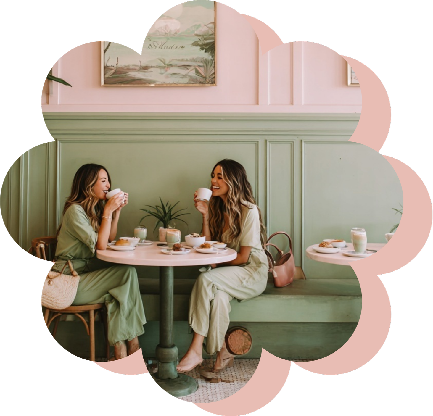 Two women sitting at a table in a cozy cafe, enjoying coffee and pastries, with pastel green walls and wall art in the background.