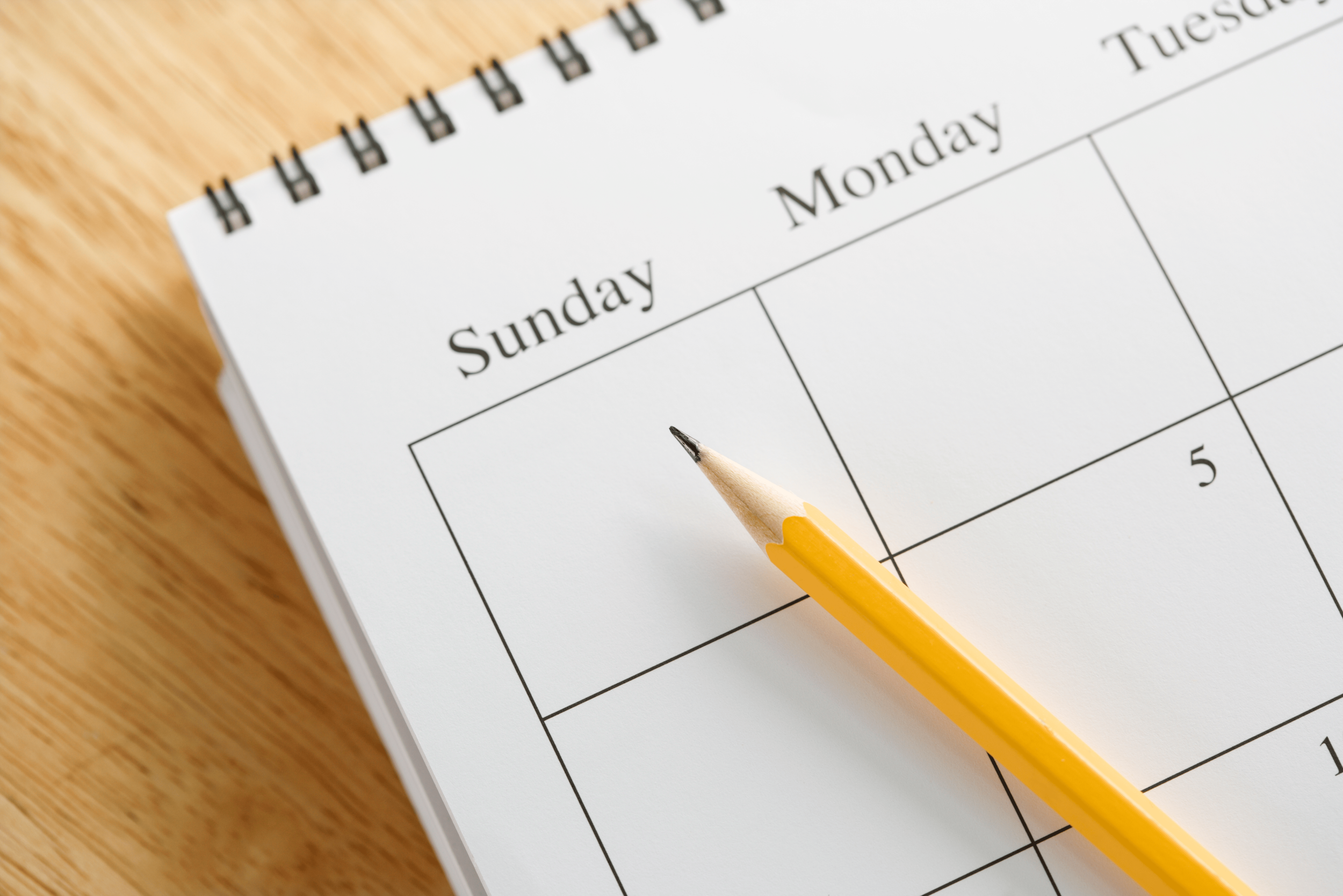 Close-up image of a weekly planner with a yellow pencil resting on the page, showing the days Sunday to Tuesday, on a wooden surface.