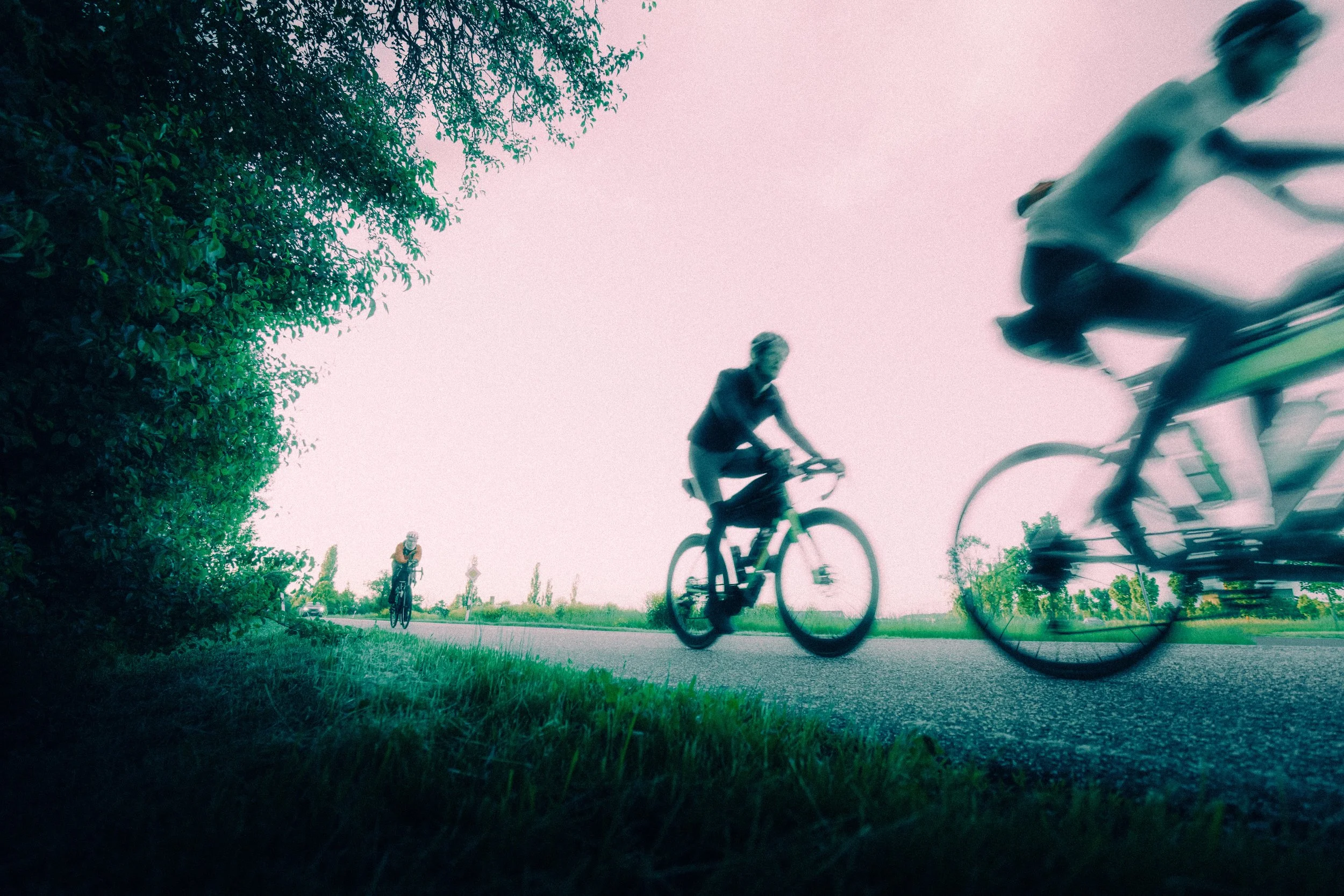 Menschen, die Fahrrad fahren, sehen von unten nach oben in die Luft, während sie auf einem Weg unterwegs sind, mit Bäumen auf der linken Seite und einem hellen Himmel im Hintergrund.