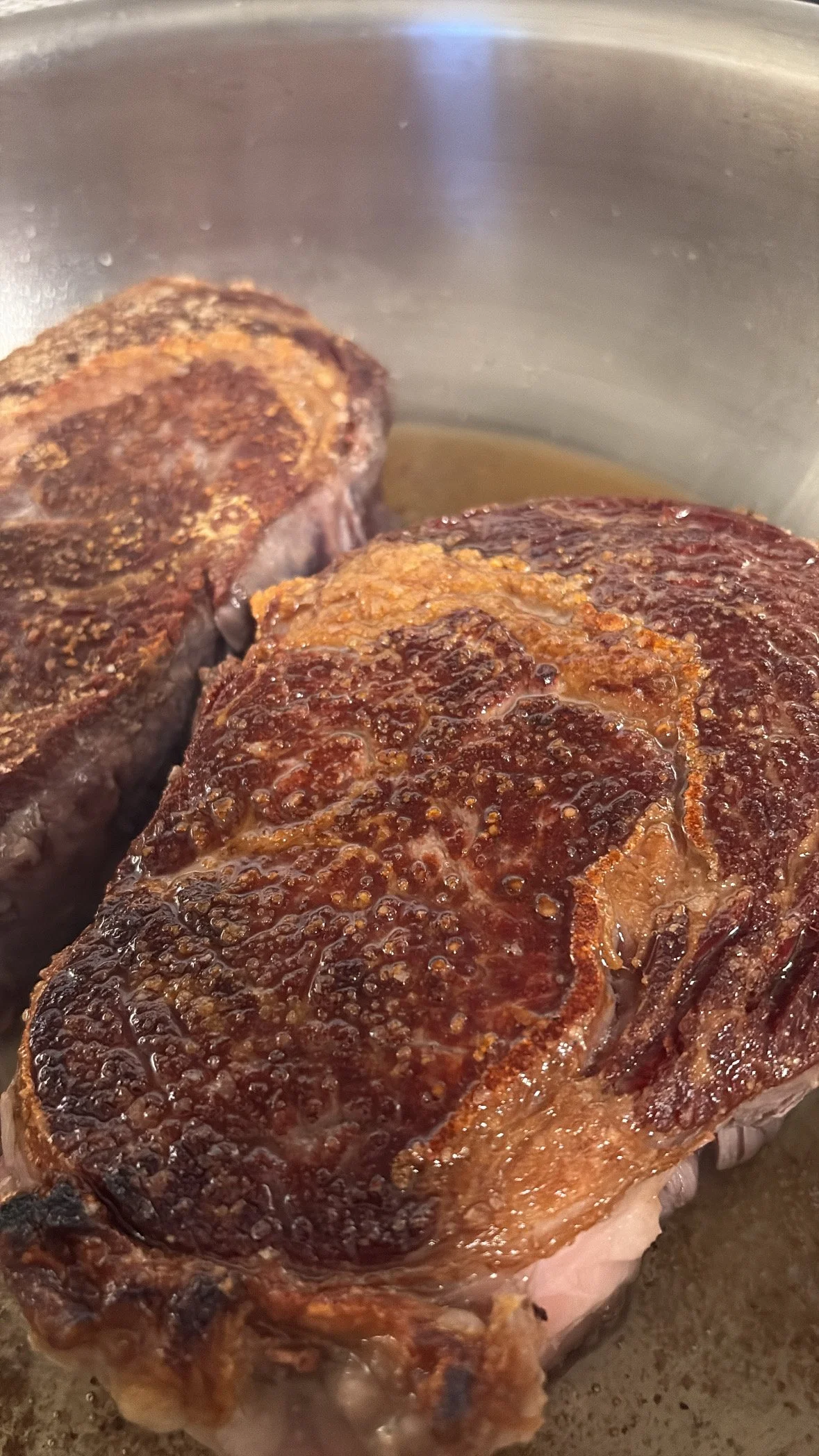 Two pieces of seared steak cooking in a pan with a browned crust.
