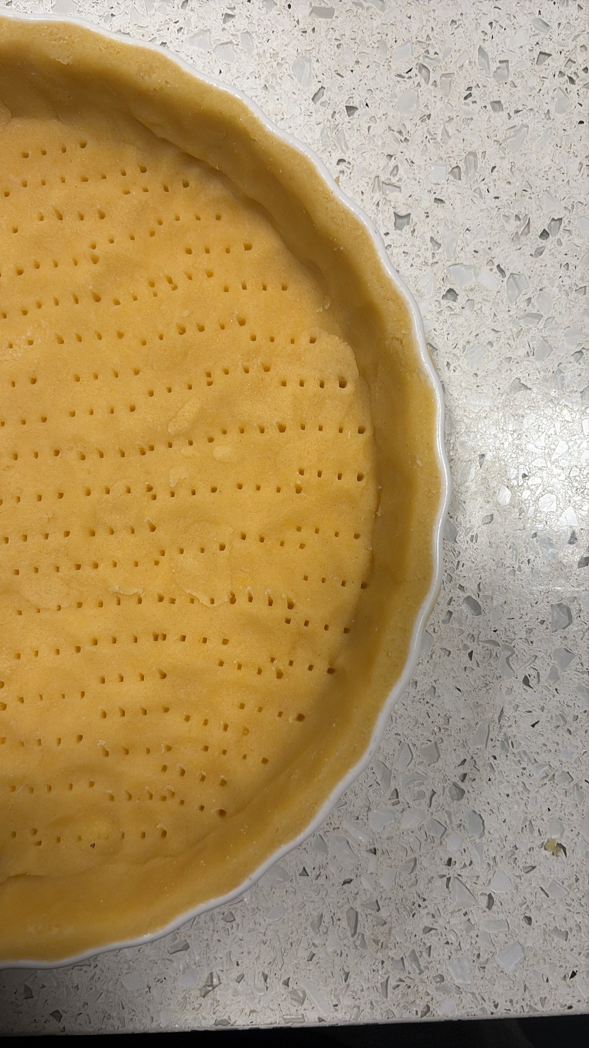 Unbaked pie crust in a ceramic pie dish on a speckled countertop.