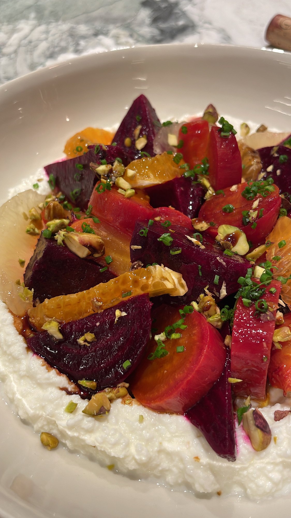 A bowl of roasted beets, orange segments, chopped pistachios, chives, and a creamy white base, possibly yogurt or ricotta cheese.