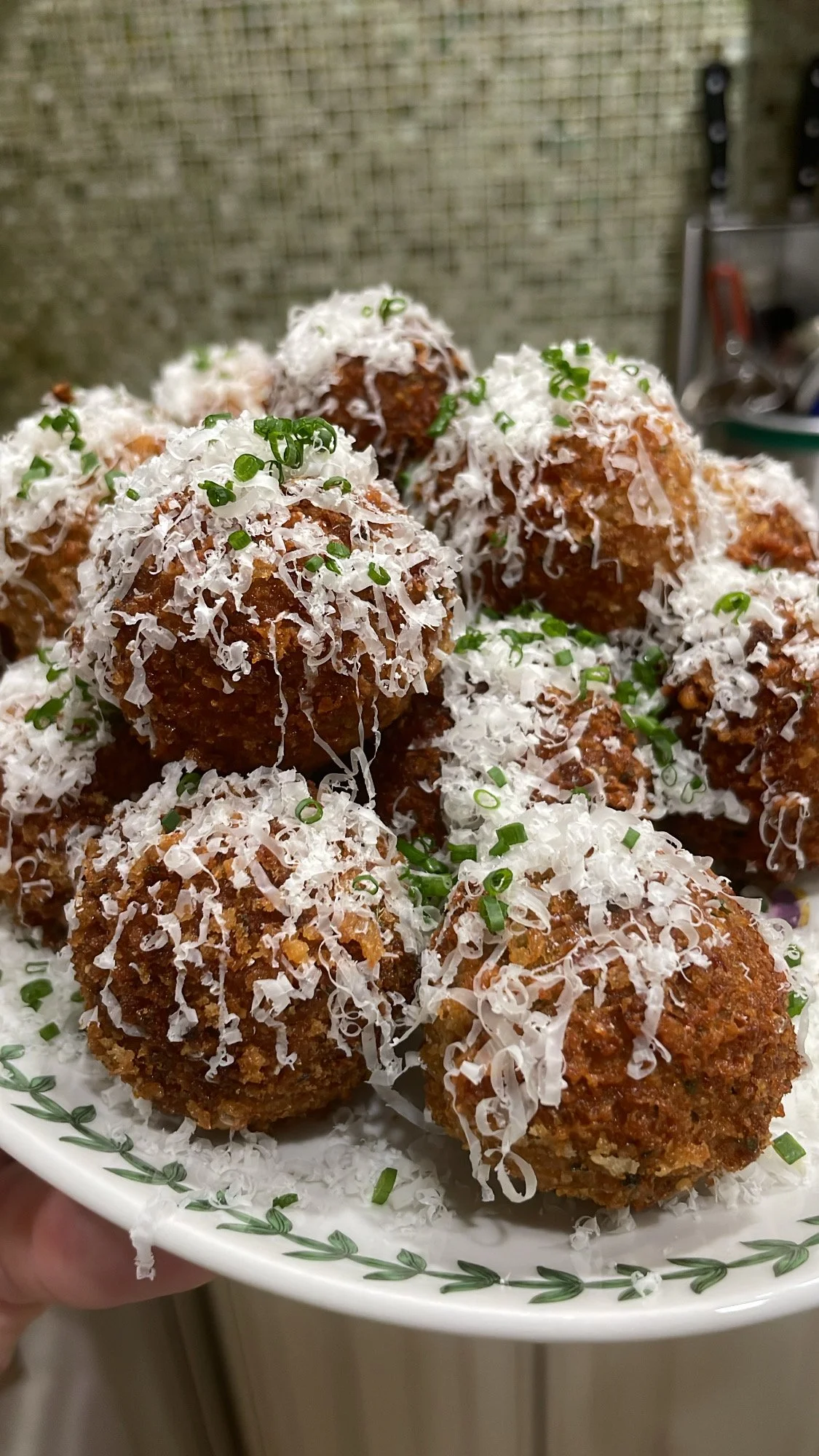 Plate of fried food balls garnished with shredded cheese and chopped chives.