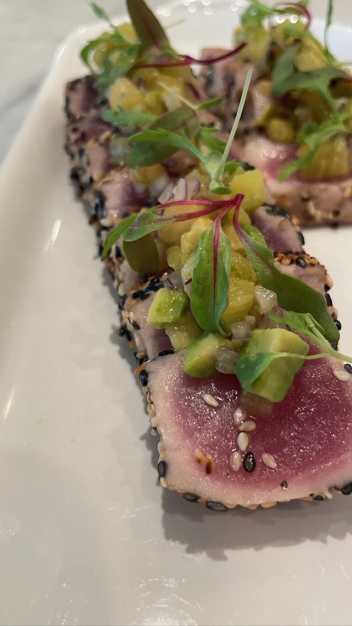 Tuna poke with sesame seeds and microgreens on a white plate
