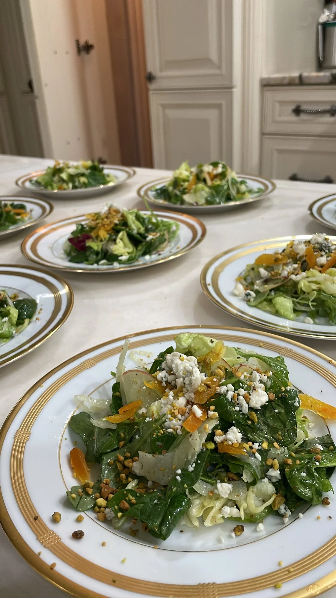 Multiple plates of salad with greens, cheese, and nuts on a kitchen table.