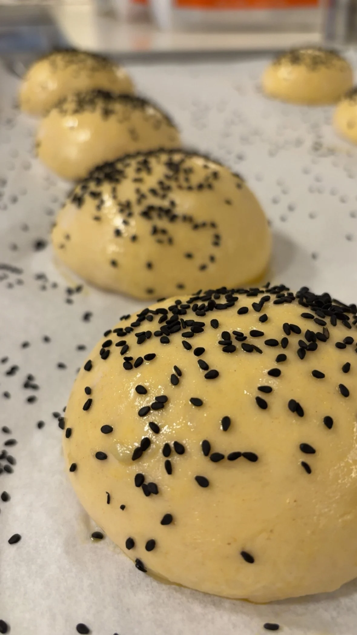 Unbaked dough balls sprinkled with black sesame seeds on a parchment-lined baking sheet.