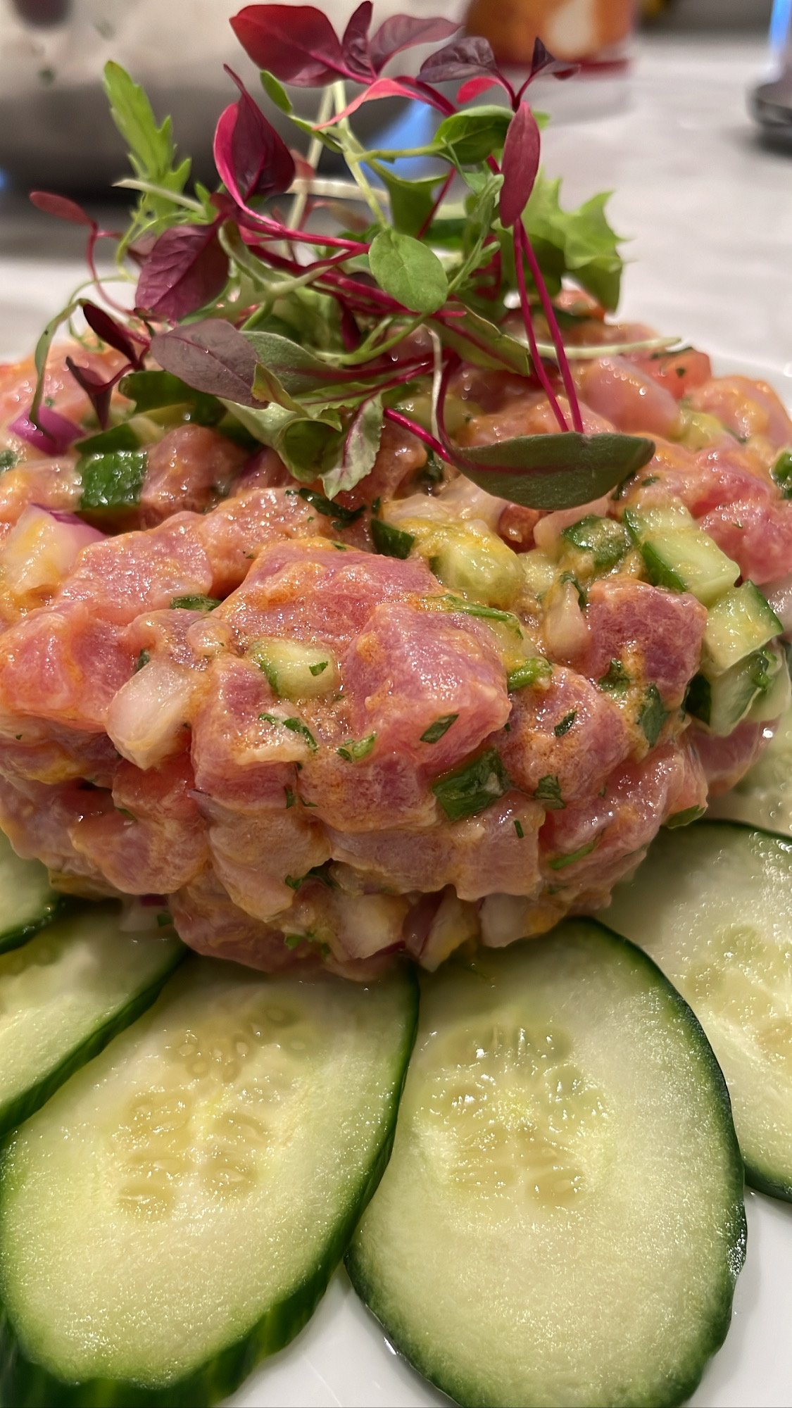 Close-up of a dish with chopped cucumber slices and a pinkish mixture topped with microgreens.