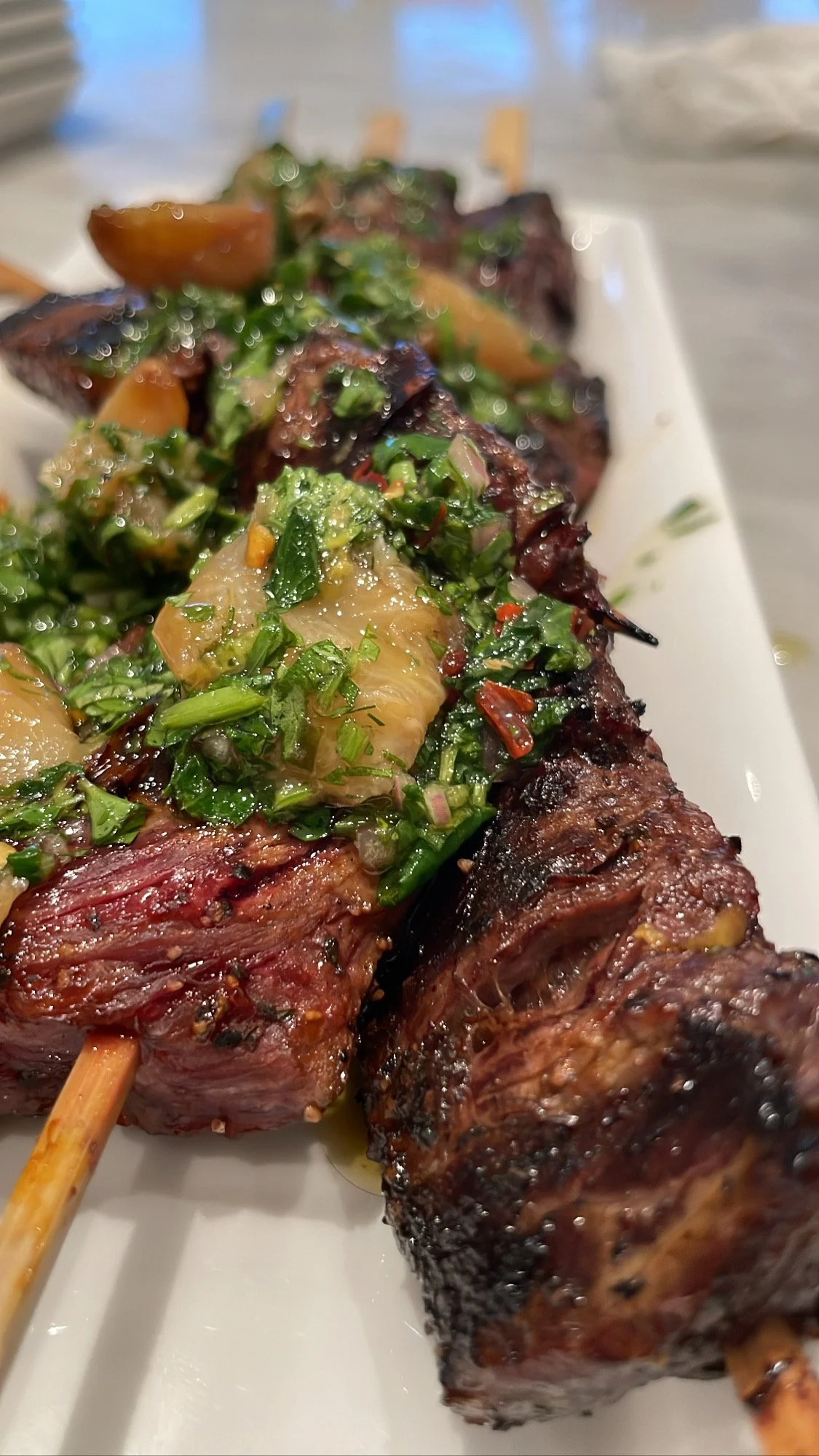 Close-up of beef kebabs topped with chopped herbs and vegetables on a white plate.
