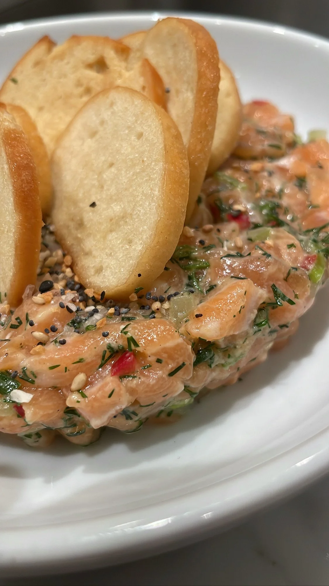 Salmon tartare topped with potato chips, served on a white plate.