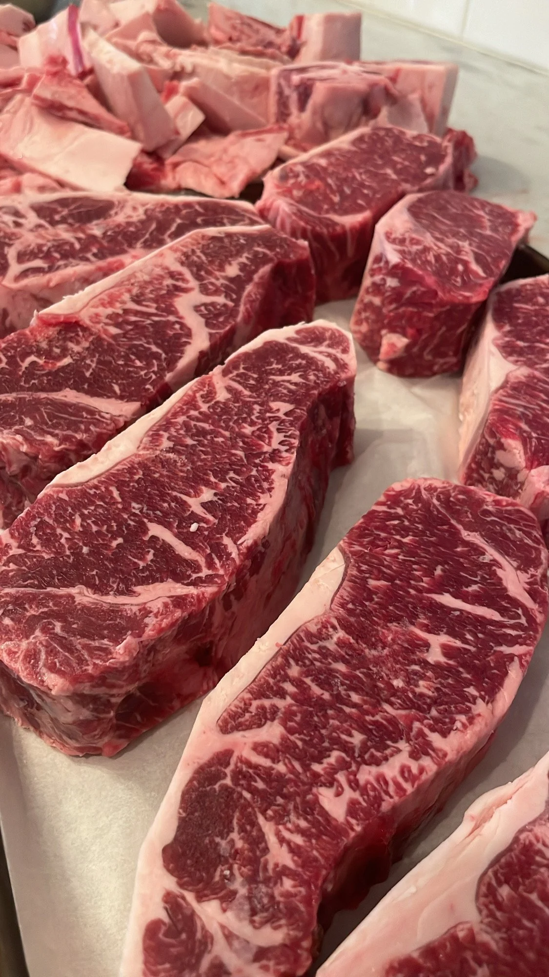 Several large, raw, marbled beef steaks arranged on a tray, displaying rich red meat with white marbling.