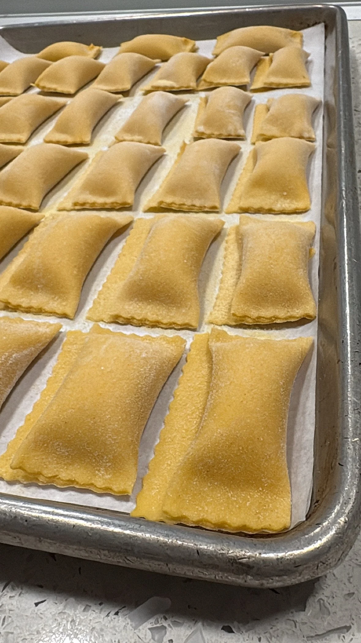 Unbaked ravioli pasta on a baking sheet lined with parchment paper.