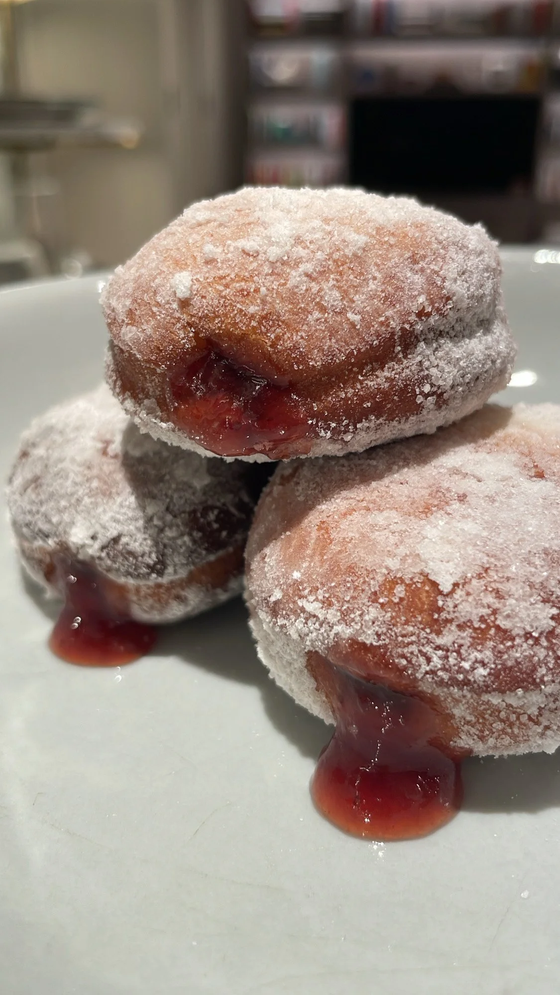 Three frozen donuts with powdered sugar and jam filling, stacked on a white plate.