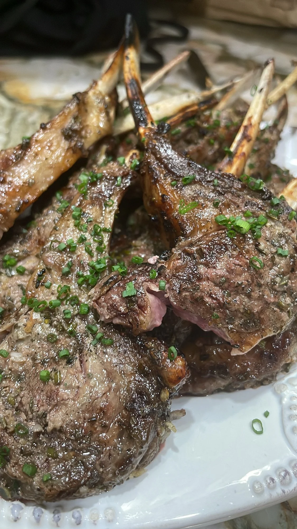 Close-up of cooked lamb chops garnished with chopped green herbs on a white platter.