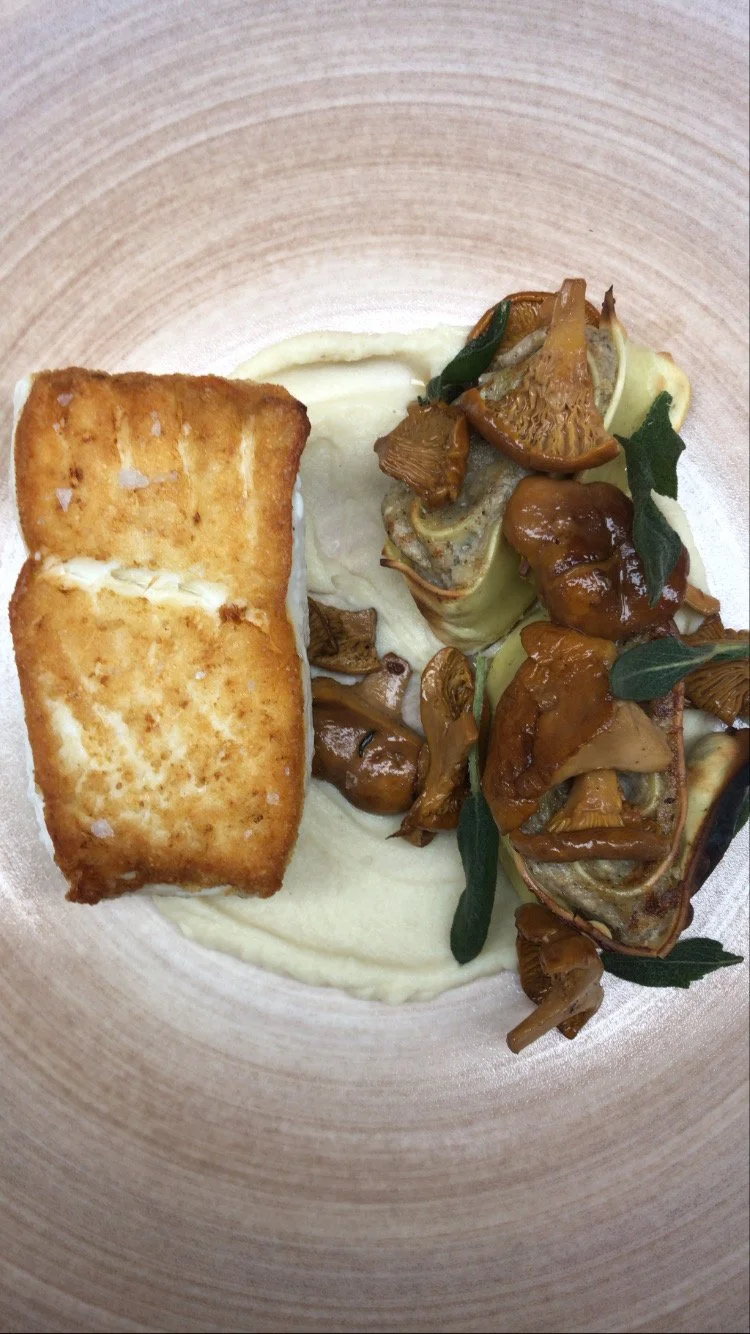 Fried fish fillet served with mashed potatoes, sautéed mushrooms, and greens on a plate.