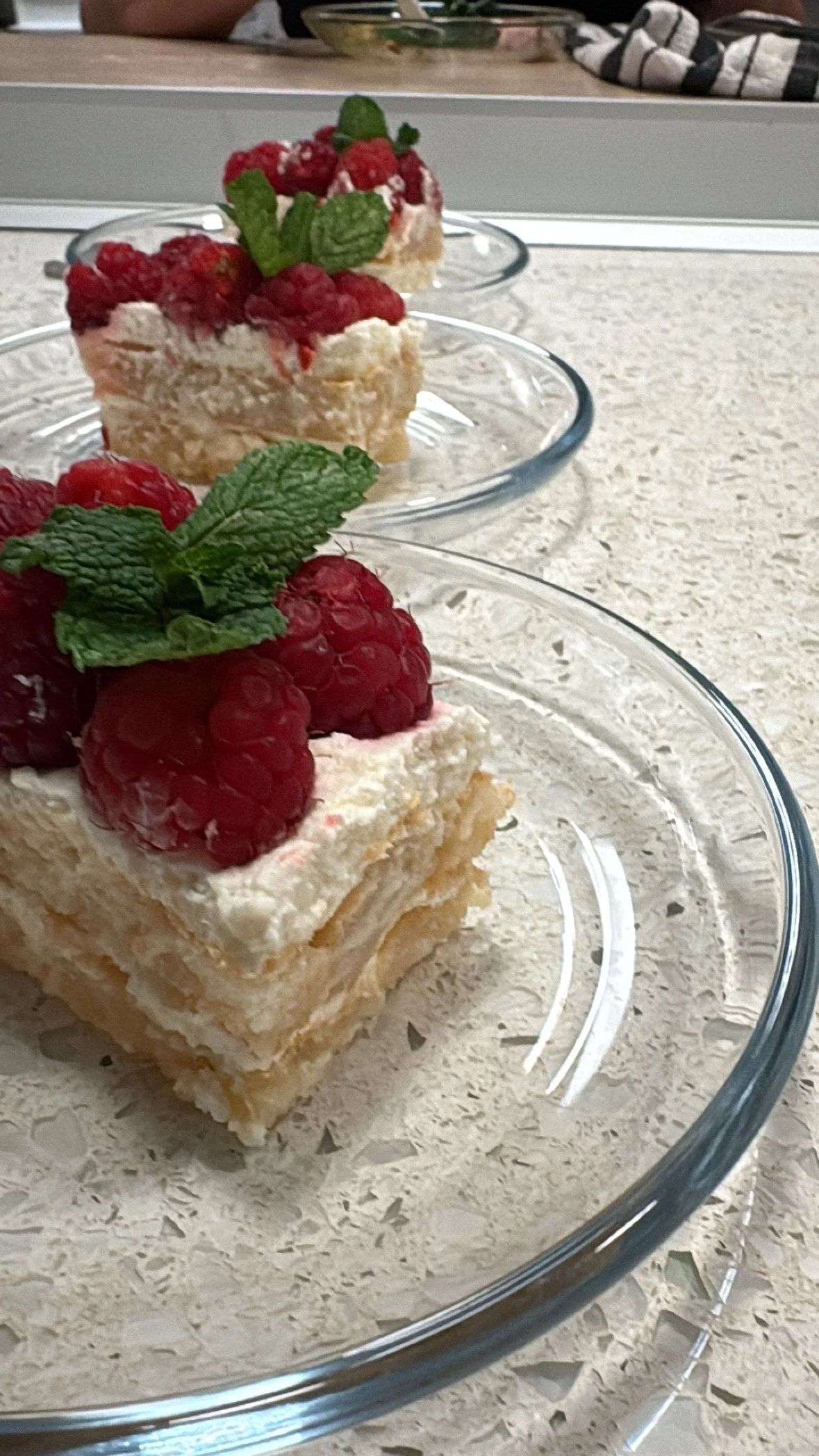 Fruit-topped layered dessert squares with raspberries and mint on top, served in glass dishes on a beige countertop.