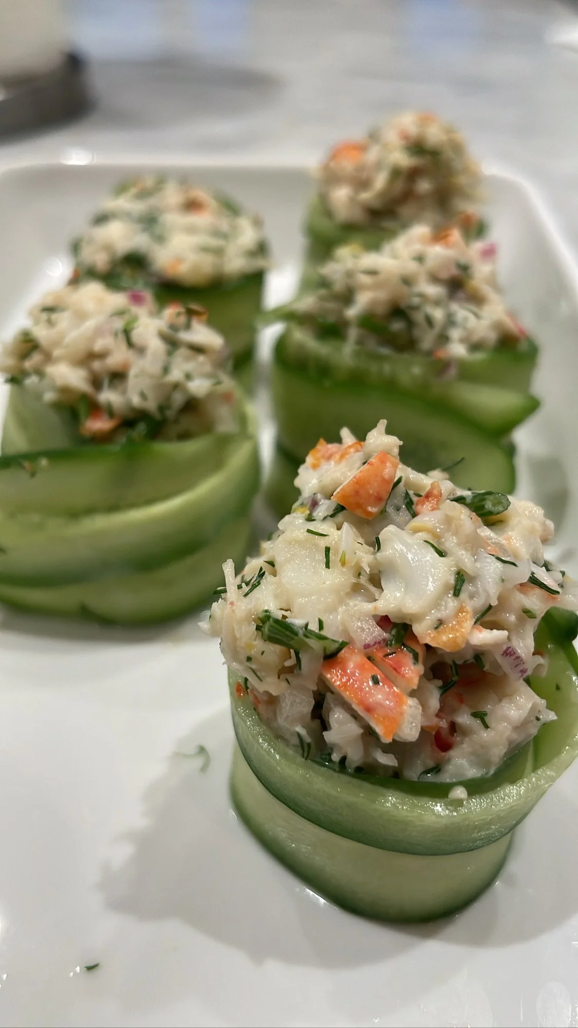 Cucumber cups filled with crab and vegetable mixture, garnished with chopped herbs.