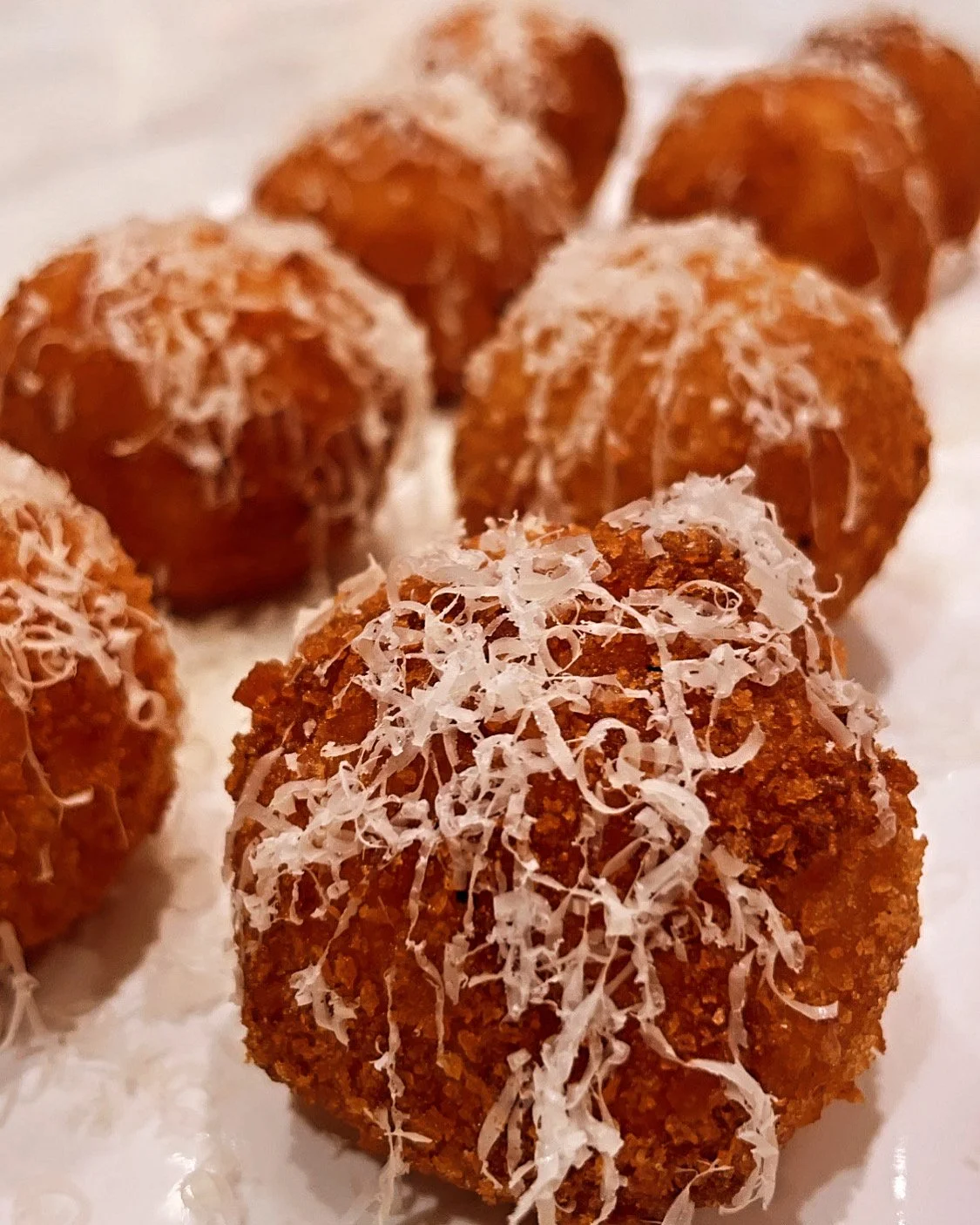 Close-up of several fried food balls topped with shredded cheese.
