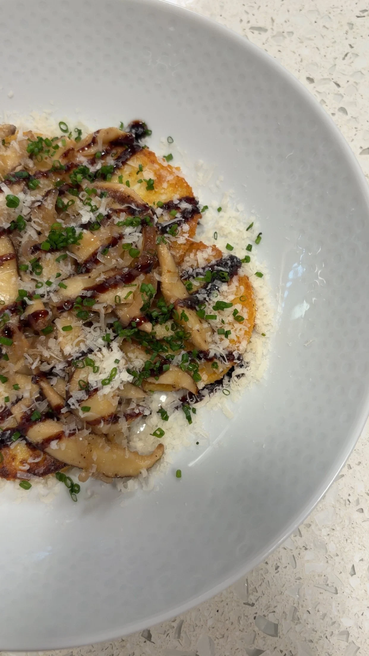 A plate of fried food topped with chopped herbs, grated cheese, and drizzled with dark sauce