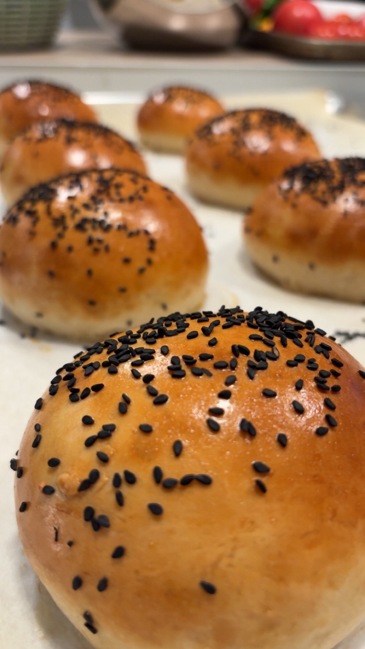 Close-up of freshly baked bread rolls topped with black sesame seeds. The rolls have a shiny, golden-brown crust.
