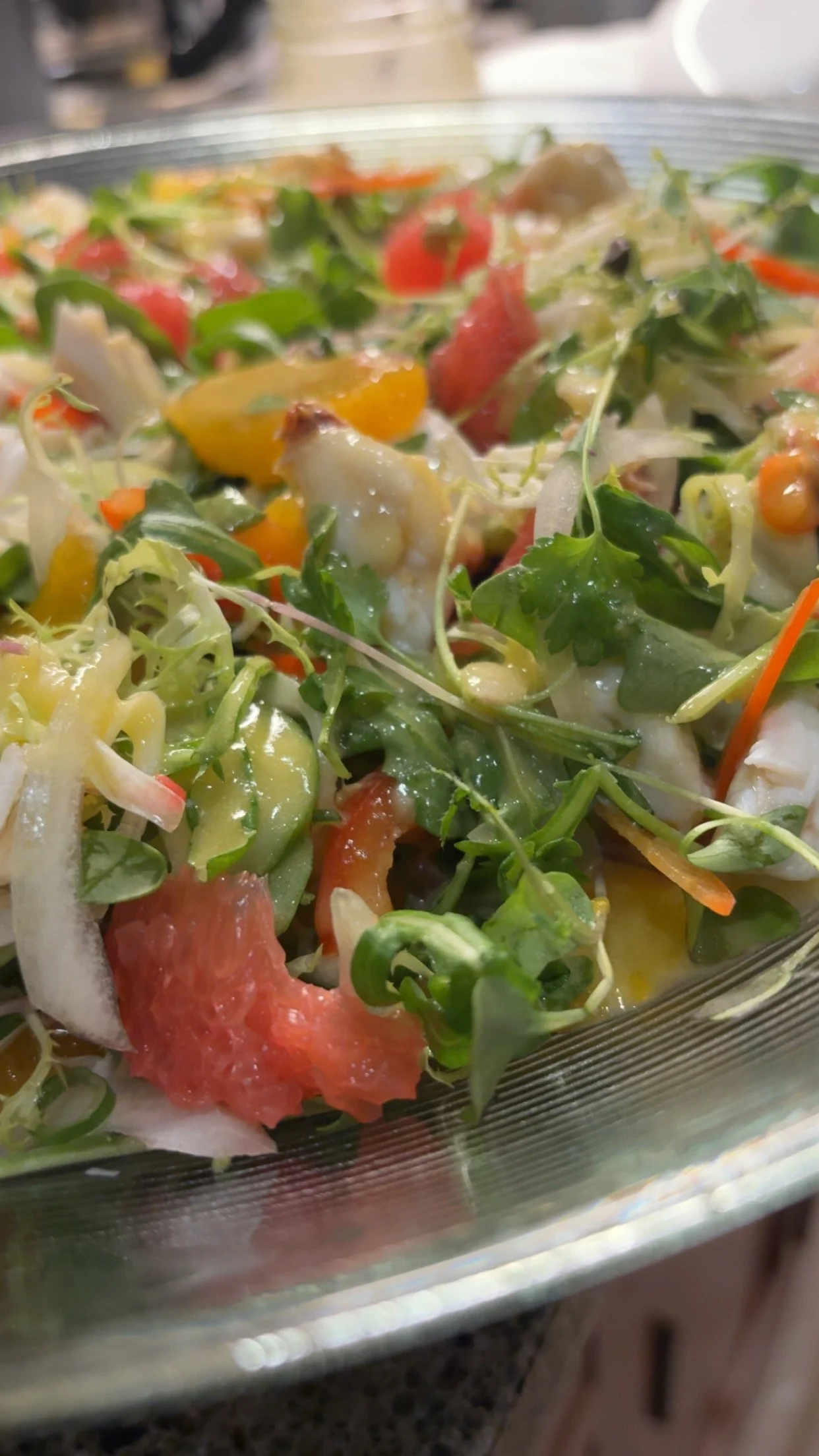 Close-up of a fresh vegetable salad with mixed greens, tomatoes, and shredded carrots in a glass bowl.
