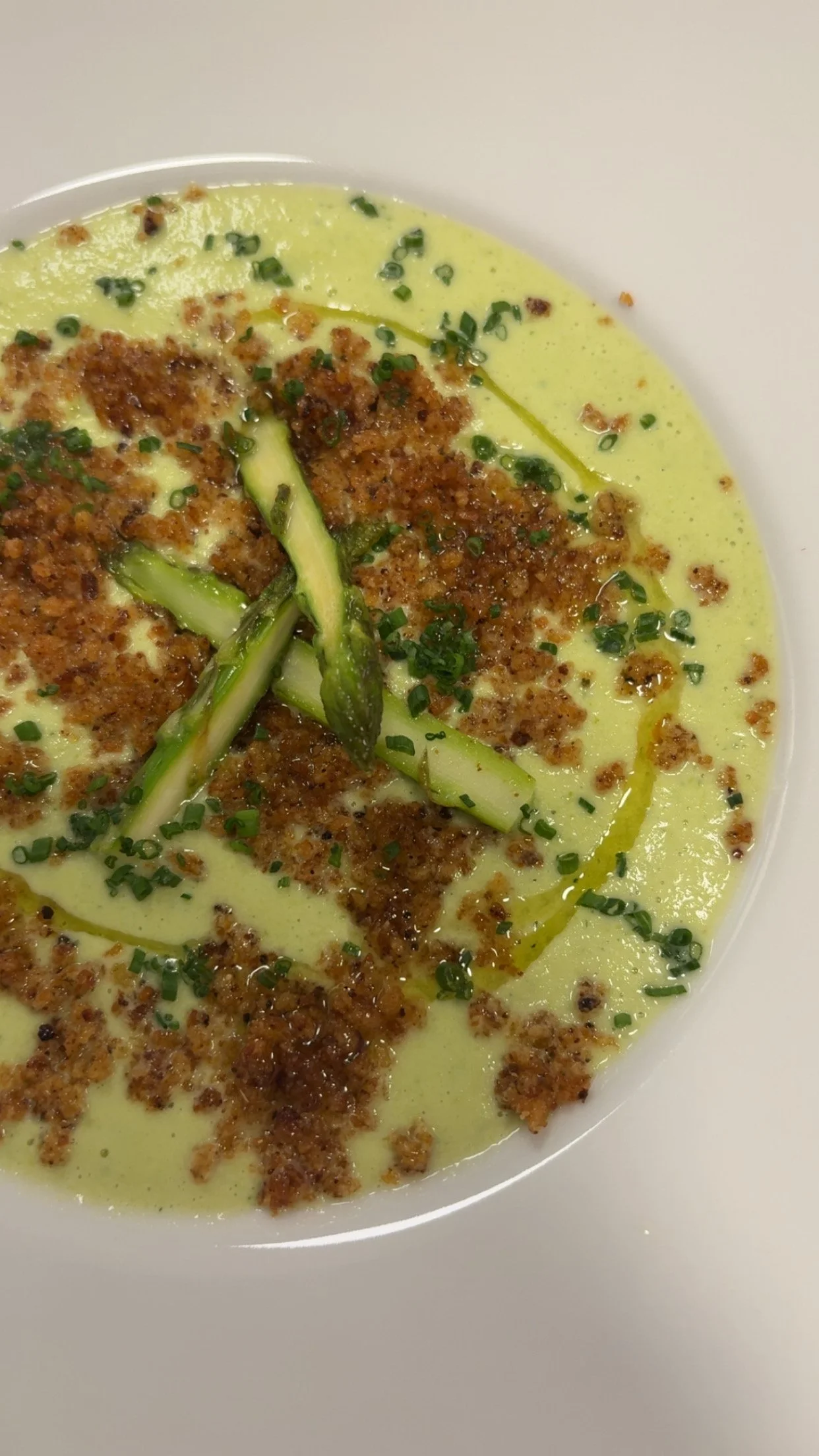 A bowl of creamy soup topped with crumbled sausage, chopped chives, and thinly sliced cucumber.