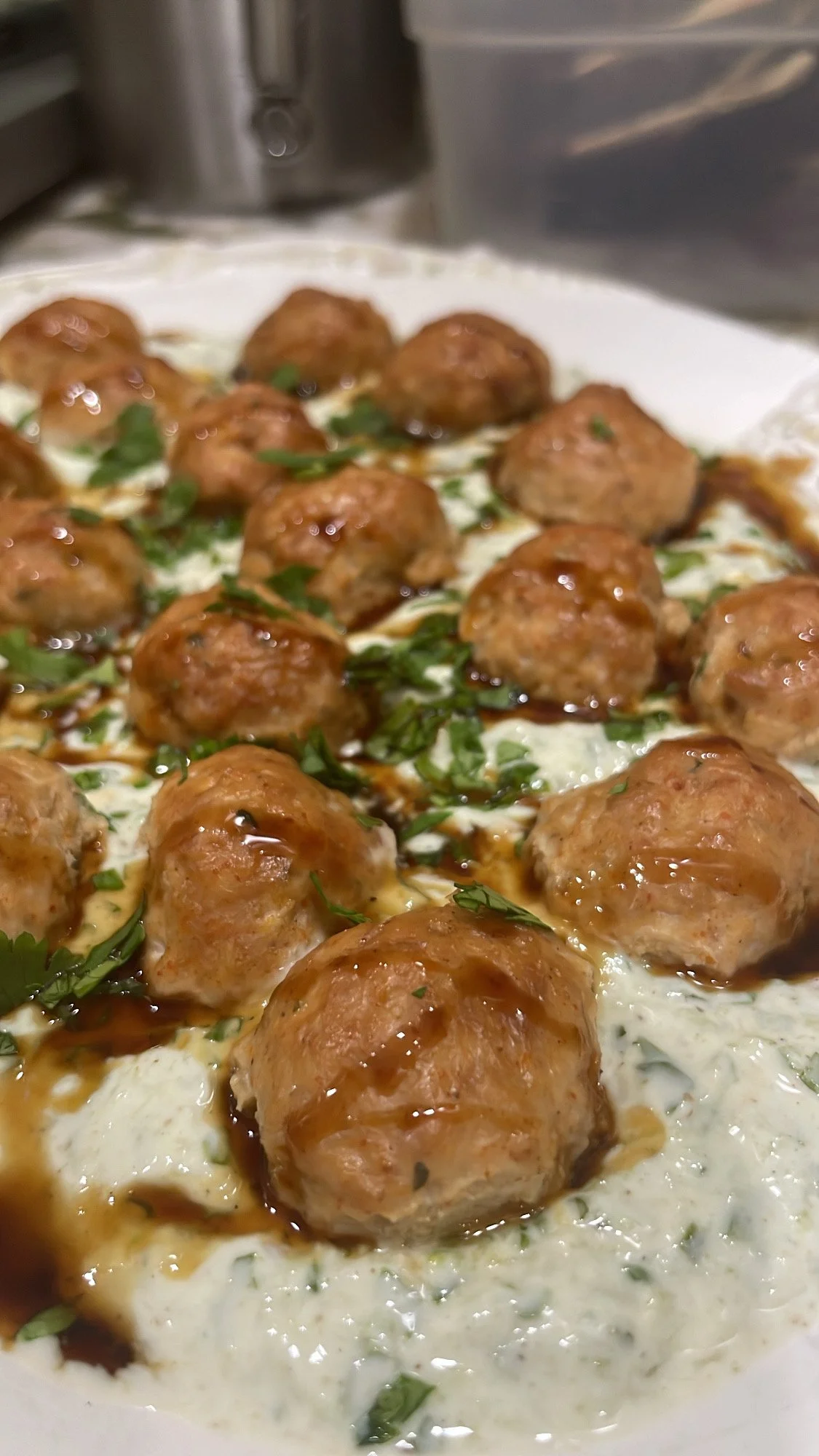 Close-up of bite-sized meatballs topped with sauce, fresh herbs, and placed on a creamy white dish.