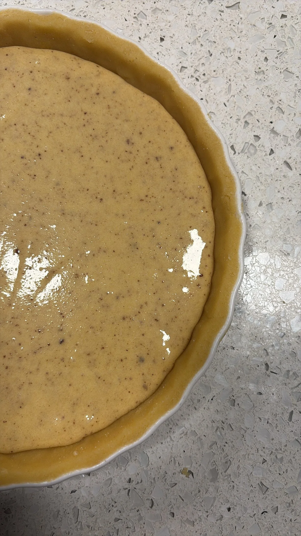 Unbaked pie crust with filling in a scalloped ceramic dish on a speckled countertop.
