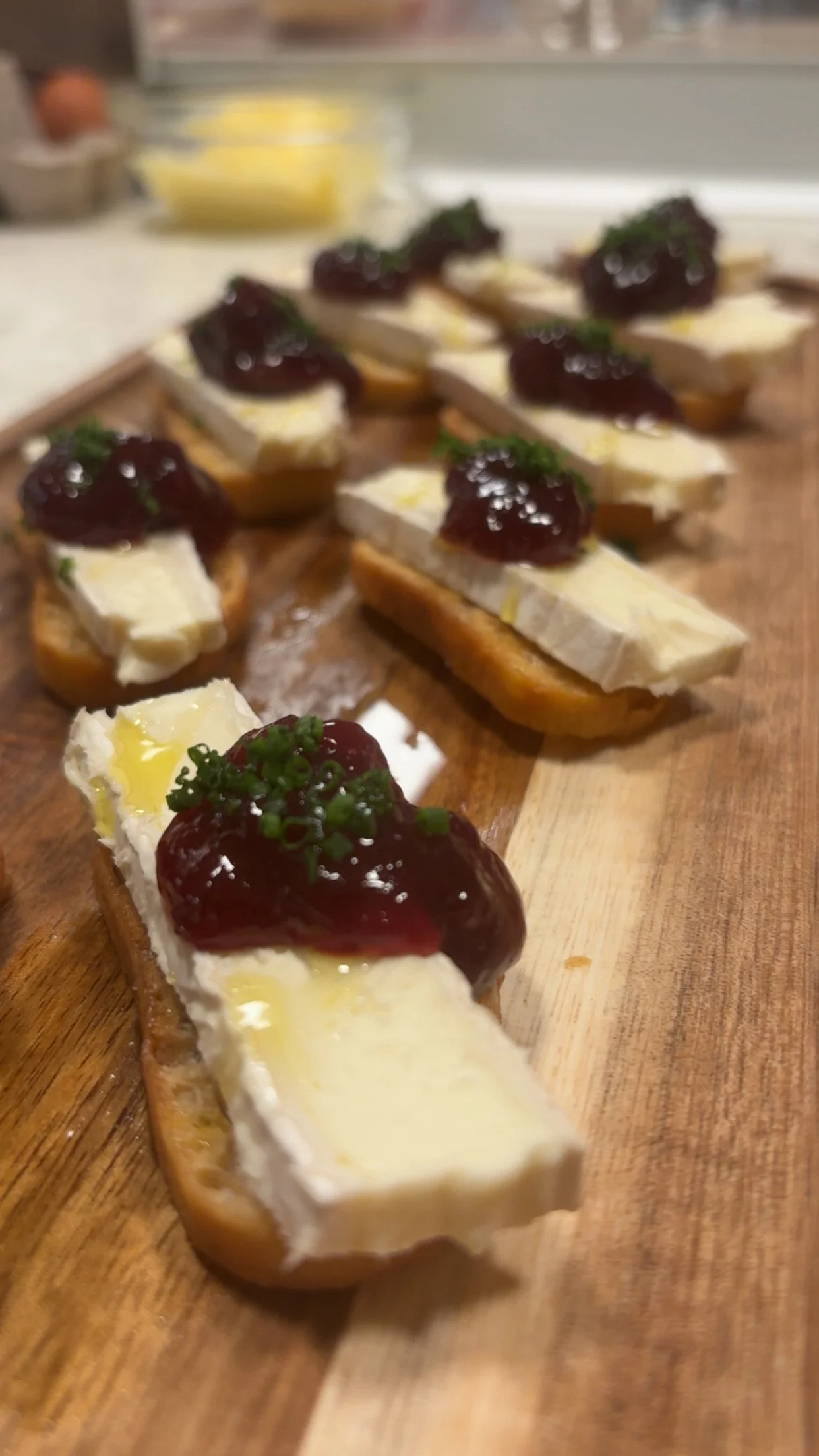 Bruschetta with cheese, cherry topping, and herbs on toasted bread slices arranged on a wooden board.