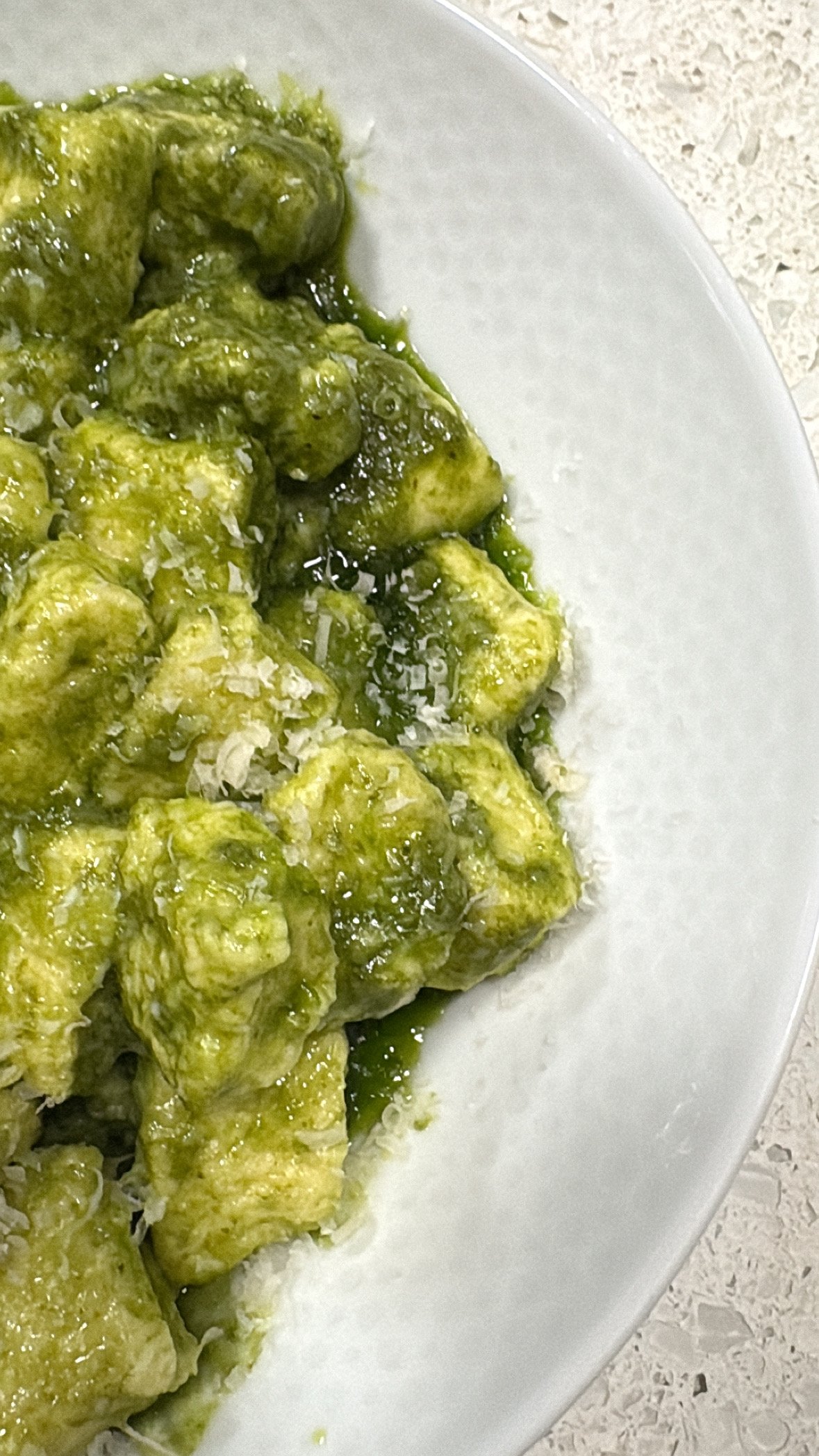 Close-up of gnocchi with green pesto sauce on a white plate.