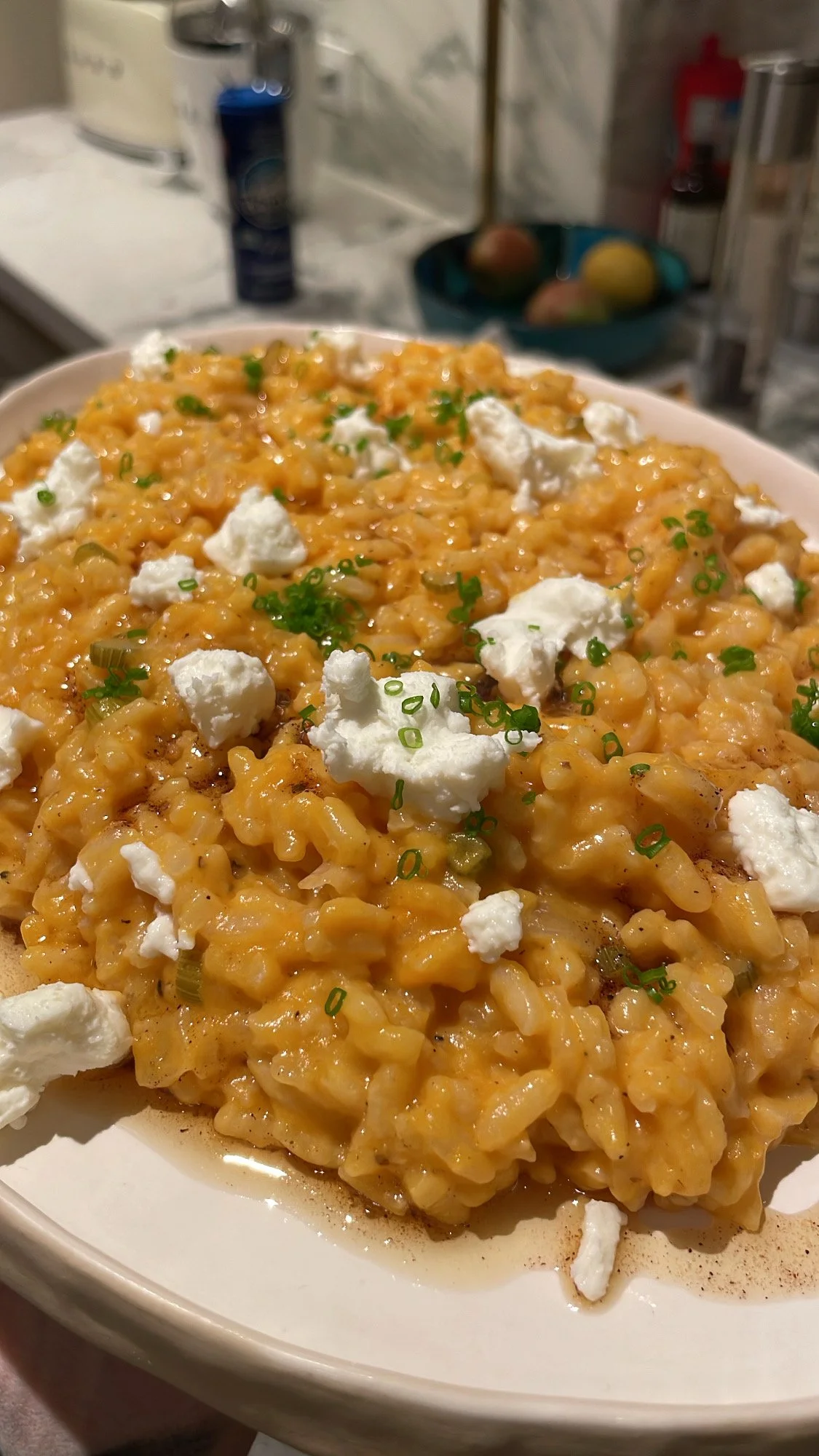 Close-up of a plate of macaroni and cheese topped with crumbled cheese and chopped green onions in a kitchen setting.