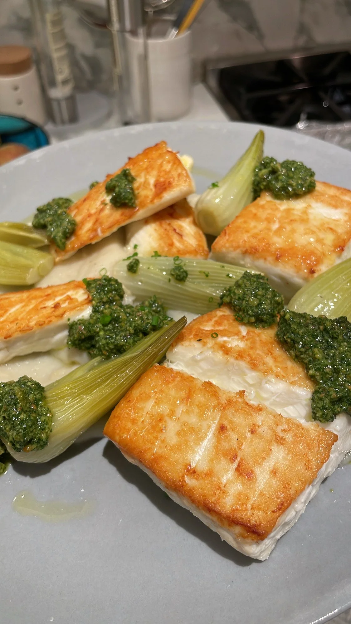 Close-up of baked halloumi cheese with grilled leeks and green pesto sauce on a grey plate.