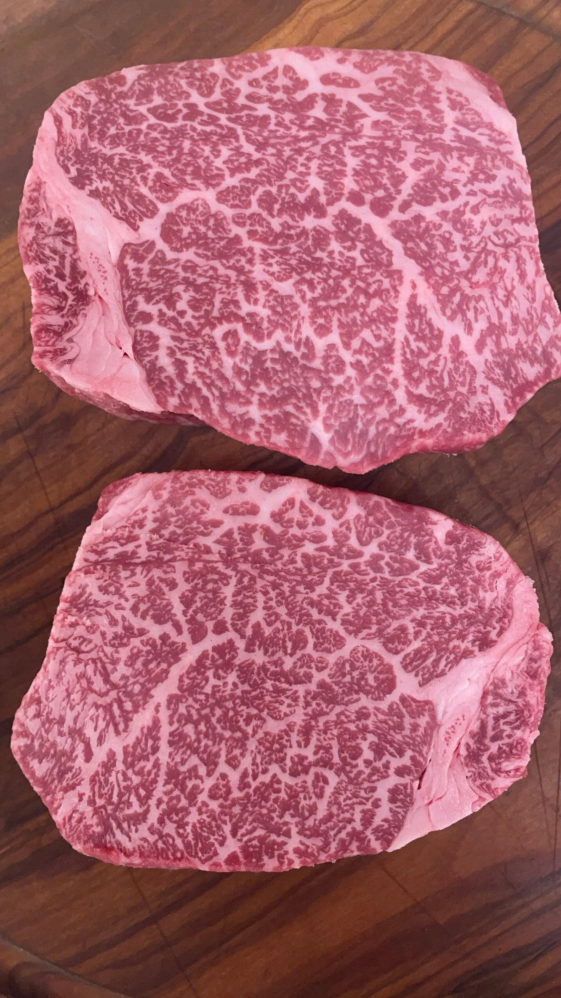 Two slices of highly marbled raw wagyu beef steak on a wooden surface.