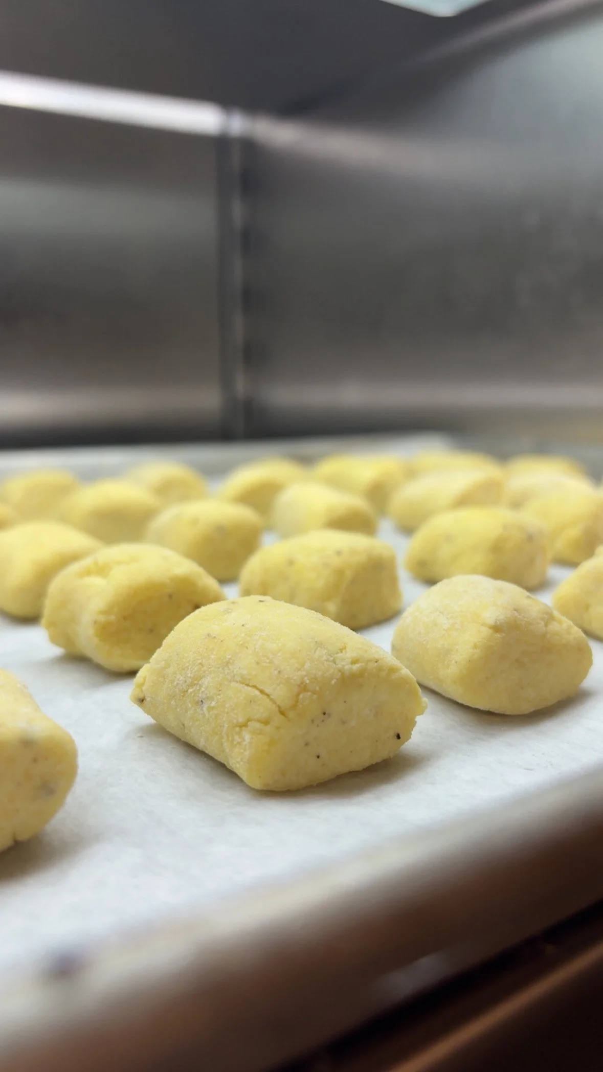 Close-up of yellow dough pieces on parchment paper inside an oven or baking tray.
