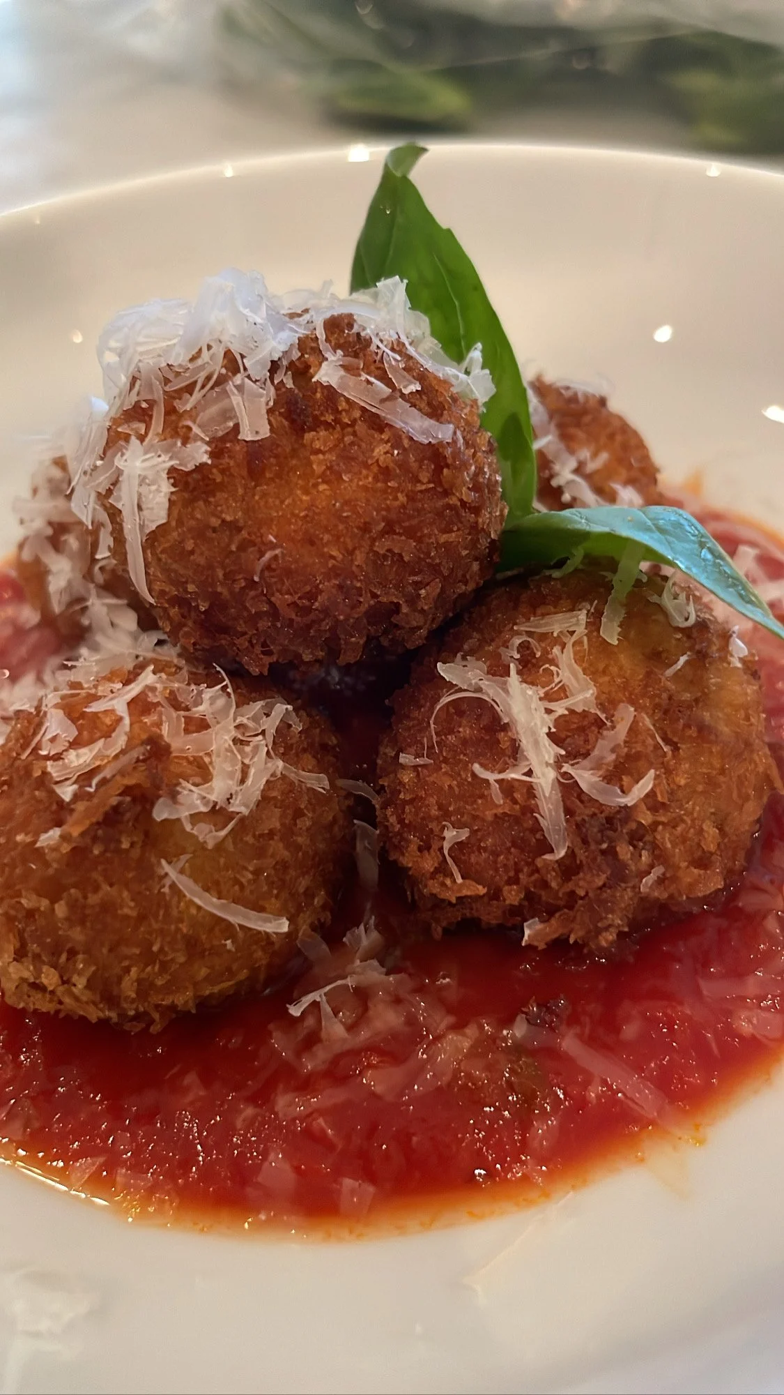 Fried arancini served on tomato sauce, garnished with basil leaves and shredded cheese.