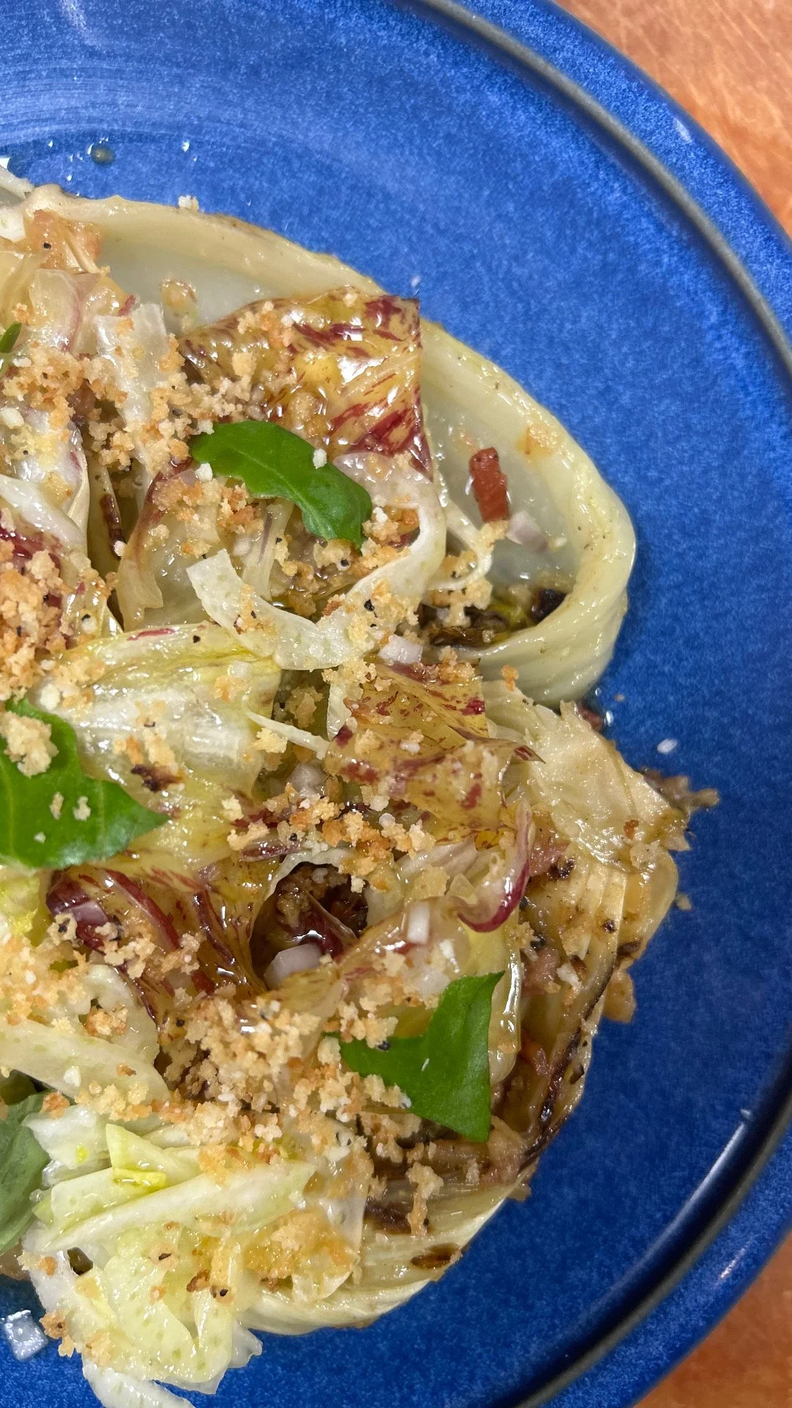 Close-up of cooked stuffed cabbage rolls topped with breadcrumbs and fresh parsley on a blue plate.