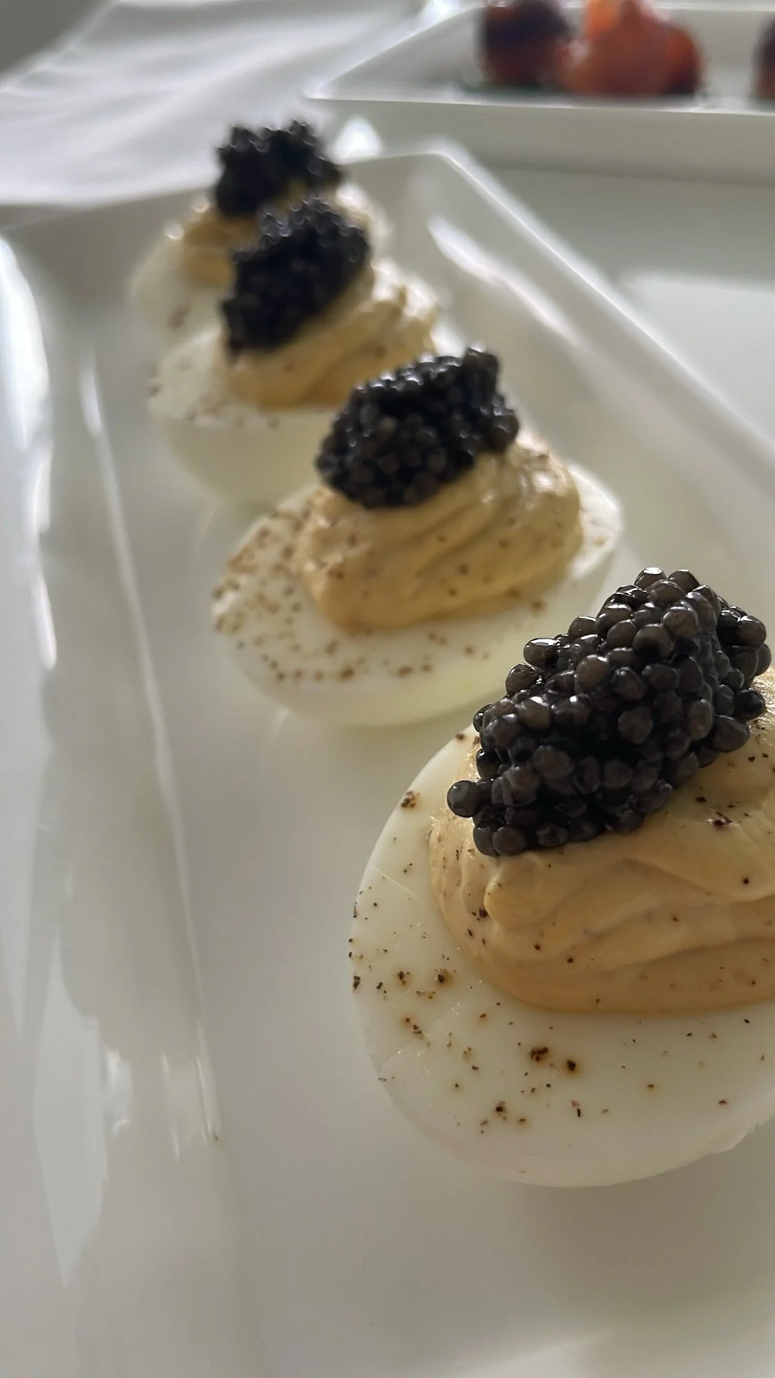 Close-up of deviled eggs topped with black caviar on a white plate.