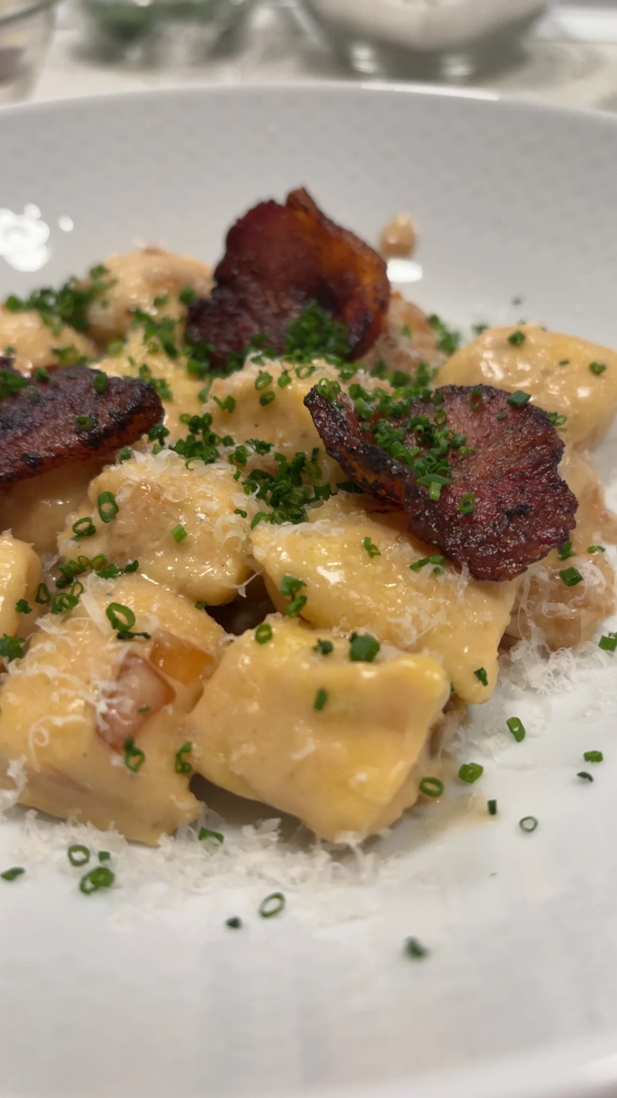 Close-up of a plate of potato gnocchi with bacon, garnished with chopped chives and grated cheese.