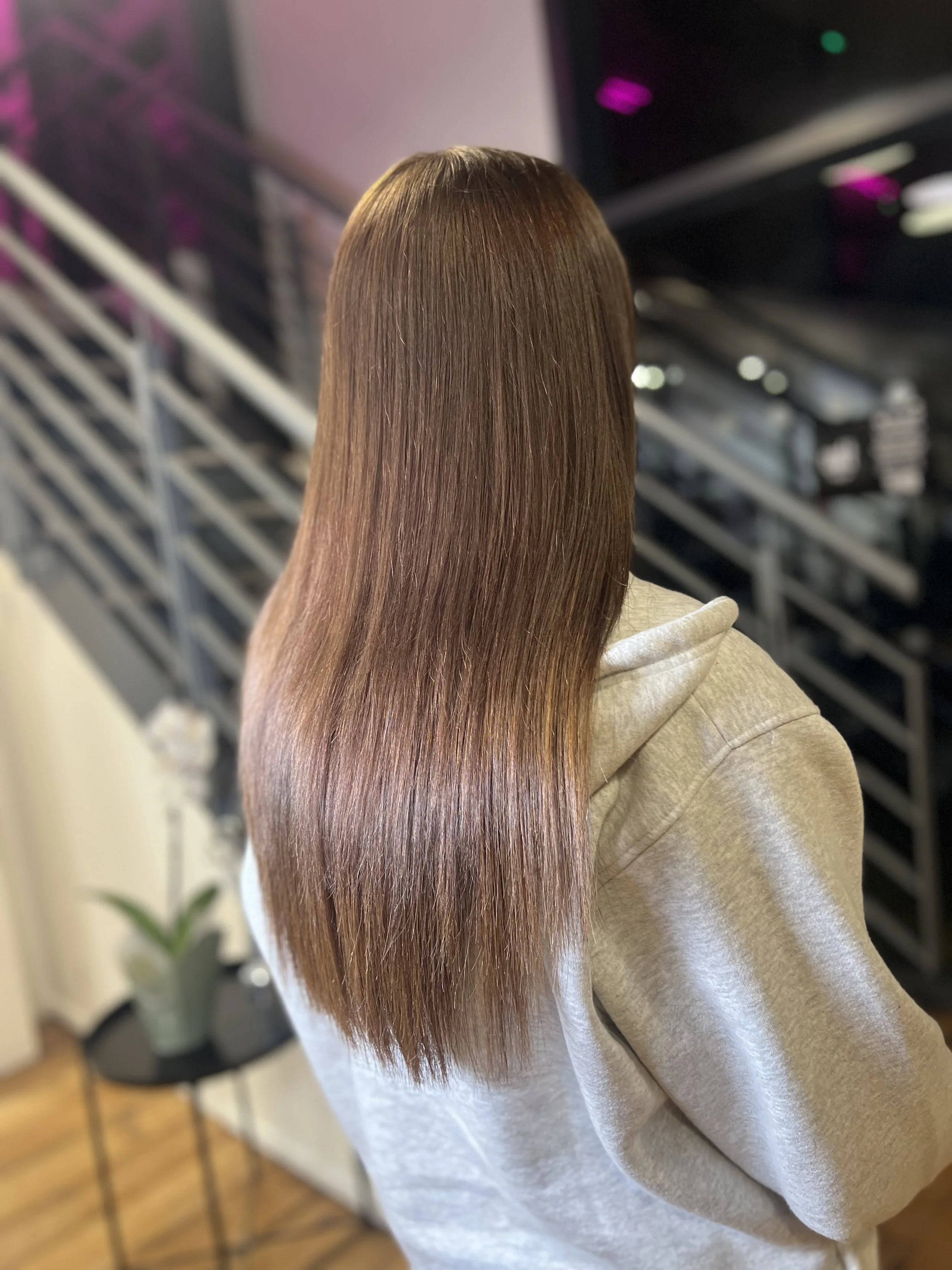 Back view of a woman with long, straight, shiny, light brown hair. Service completed by Hair Stylist