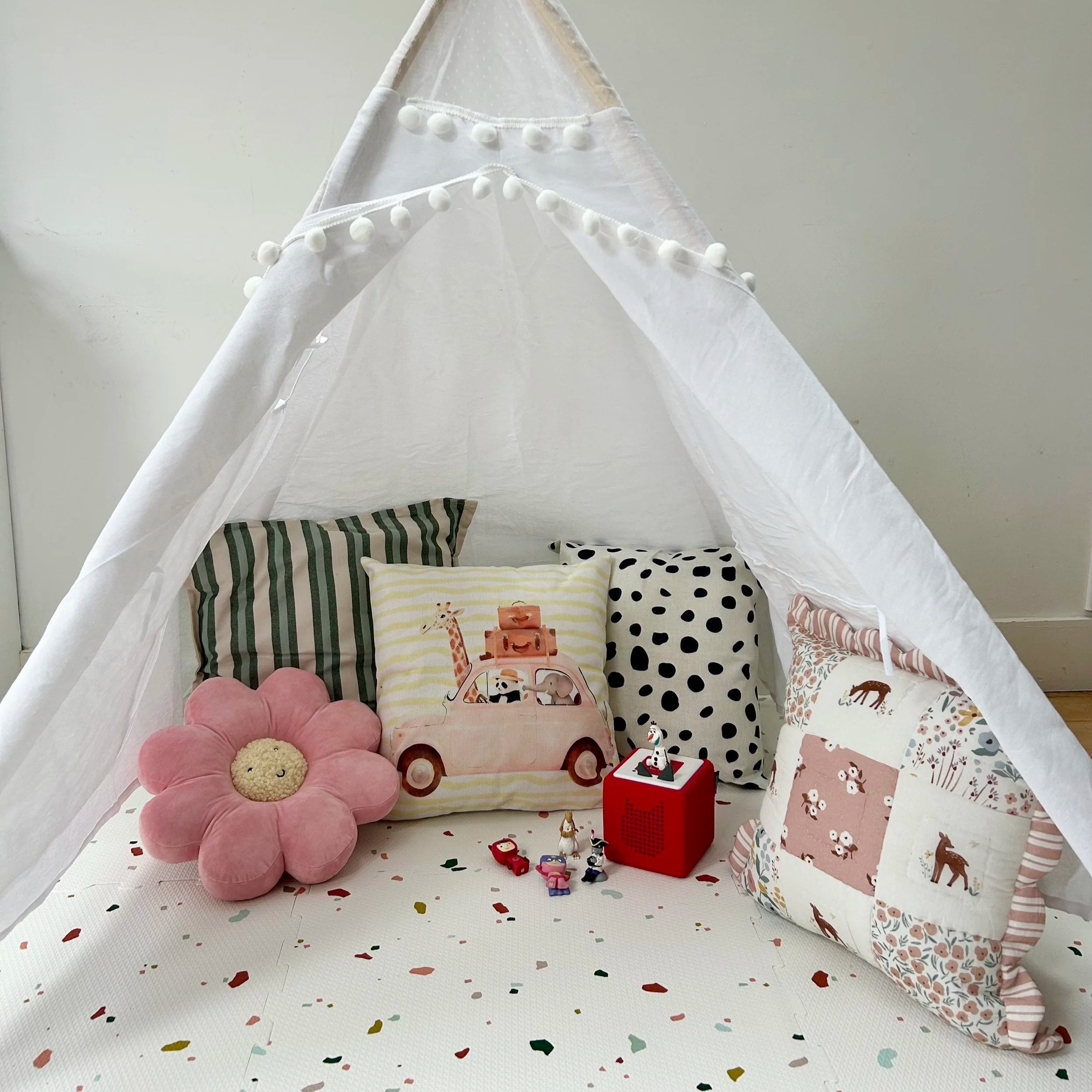 Children's play area with a white teepee tent, colorful pillows, plush toys, and small figurines.