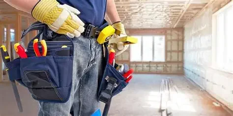 Construction worker with tool belt holding a level at an indoor construction site.