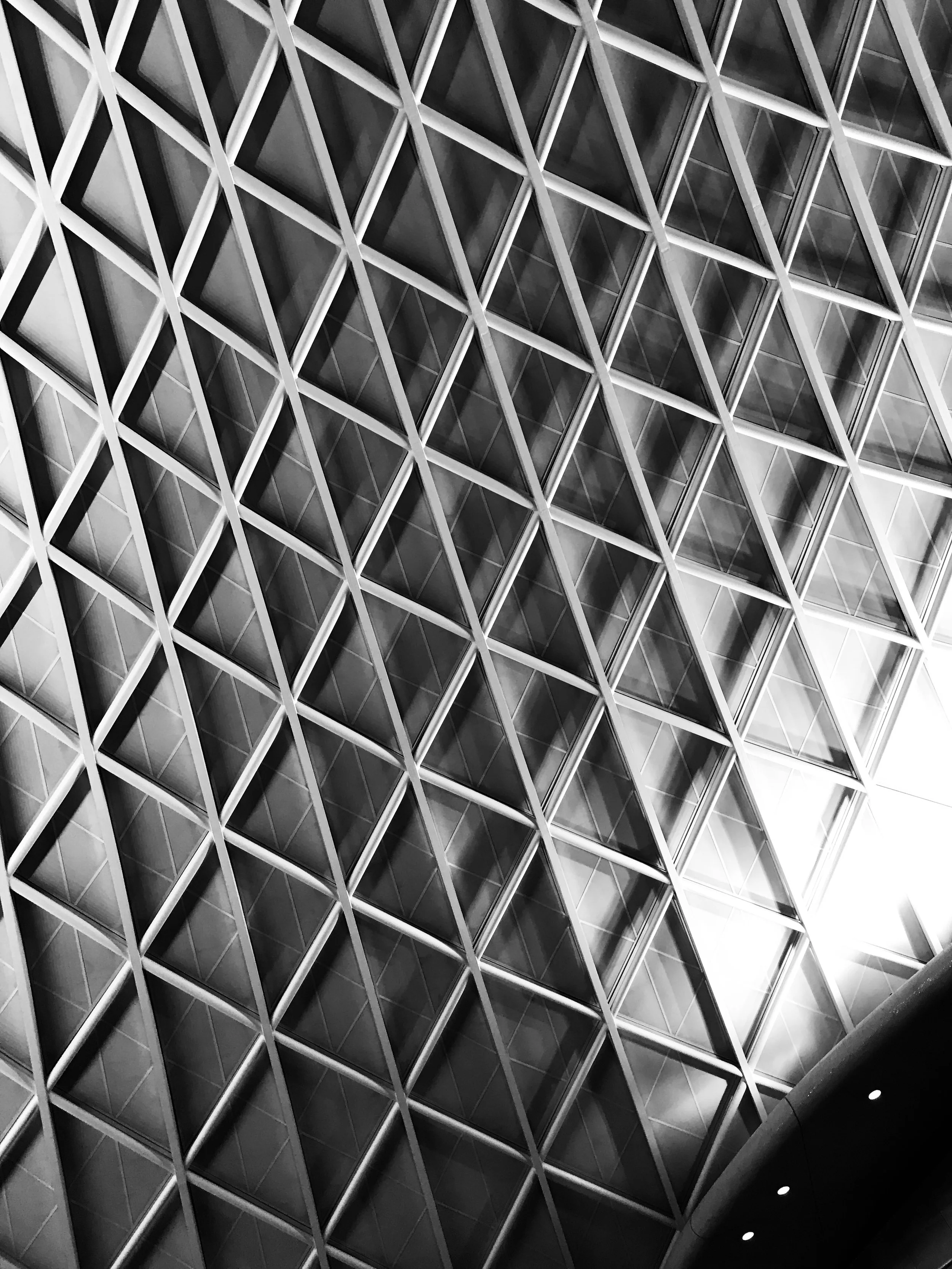 Close-up of a modern building facade with a geometric pattern of diamond-shaped glass windows and metal framework, viewed from below.