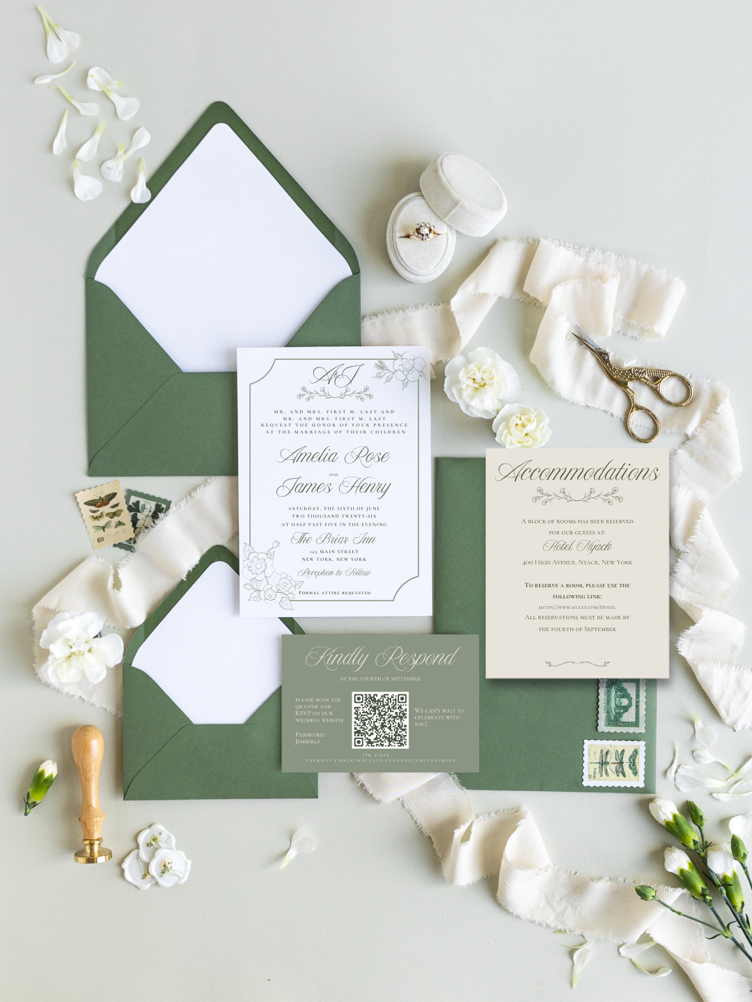 Wedding invitation suite with green envelopes, white RSVP card, and details card, surrounded by white flowers, a pair of scissors, a ring box, postage stamps, a wax seal stamp, and decorative flower petals on a light background.