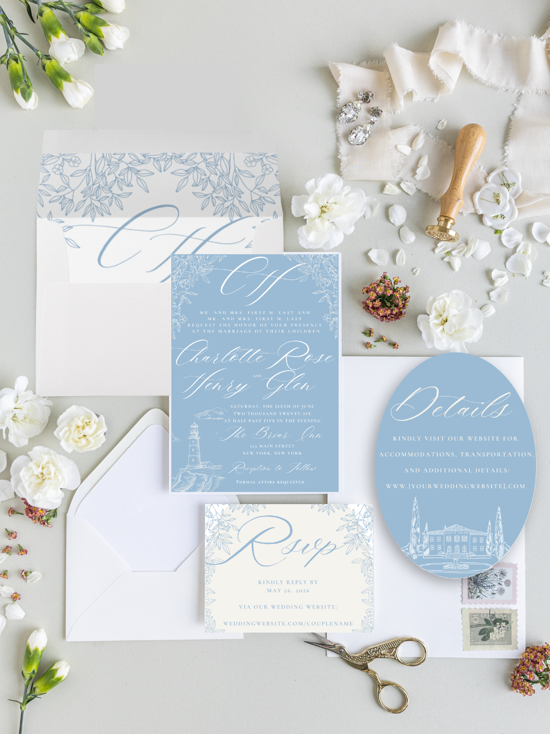 A wedding invitation suite with matching envelope and RSVP card, adorned with a lighthouse illustration, surrounded by white flowers, jewelry, a wax seal stamp, and vintage scissors, all on a light-colored background.