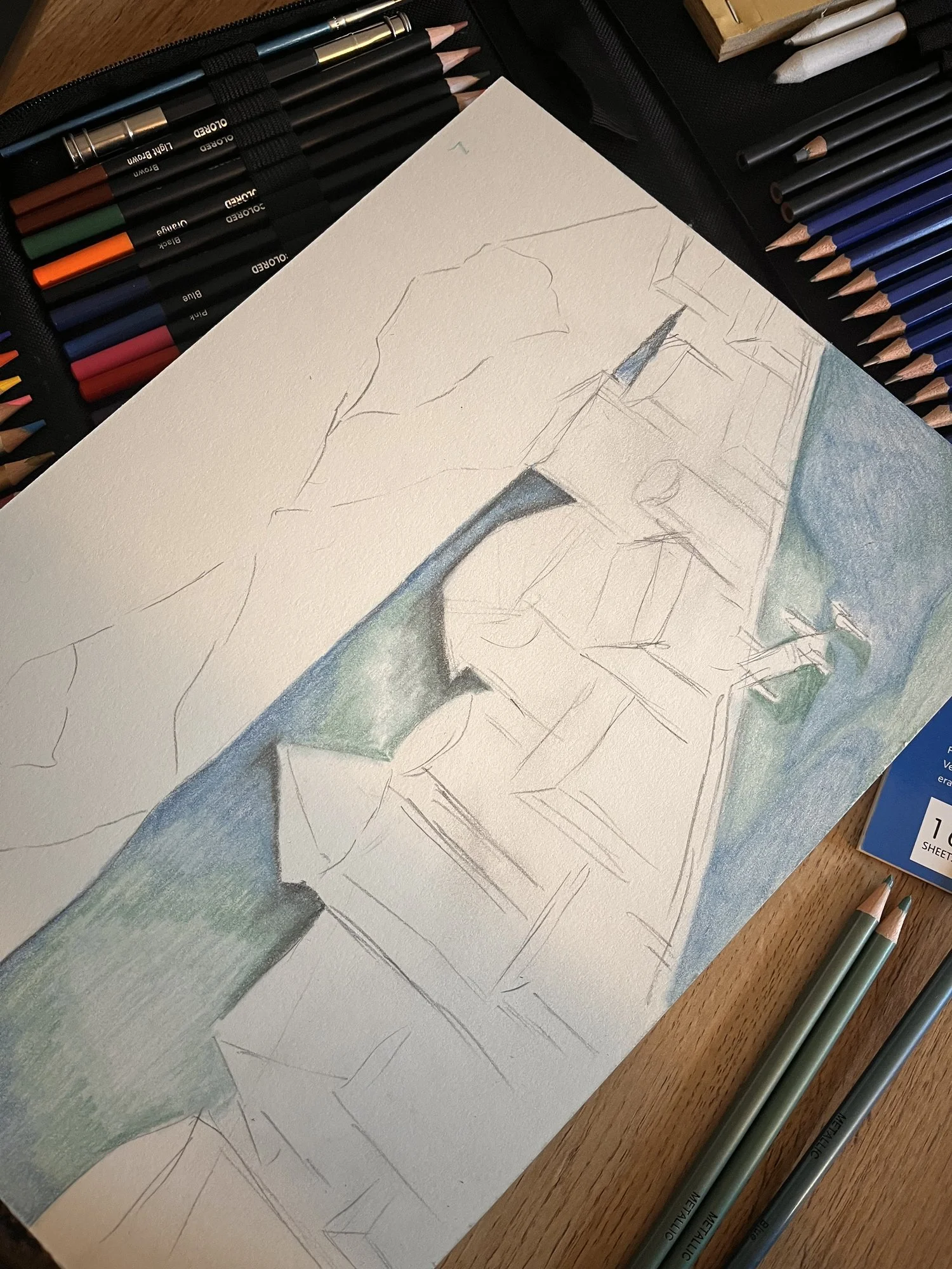 Erste Bleistiftlinien einer Landschaft auf Papier, daneben Buntstifte